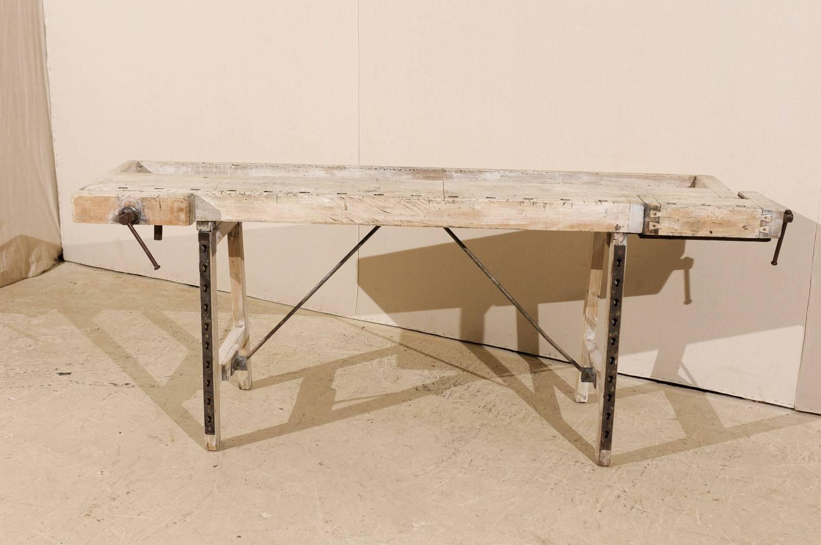 A Swedish 19th century shop bench table with adjustable side clamps. This table has some light accents of off-white paint throughout with some natural wood coming through.
