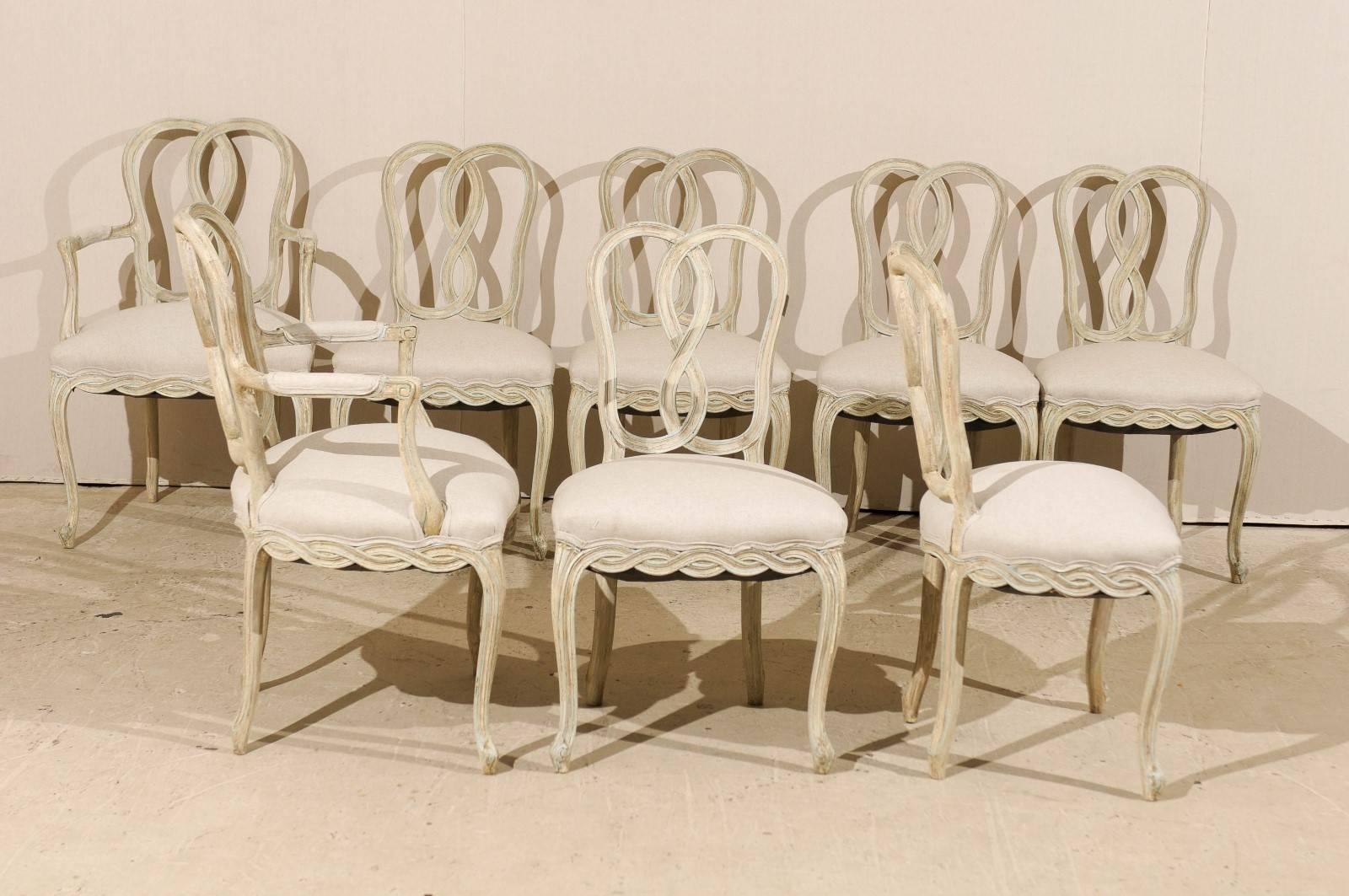 A set of eight Italian Venetian style painted wood chairs. This set of two armchairs and six side chairs feature intertwined ribbon motifs on their backs and skirts. The chairs also have cabriole legs. This set has a grey / cream color with light