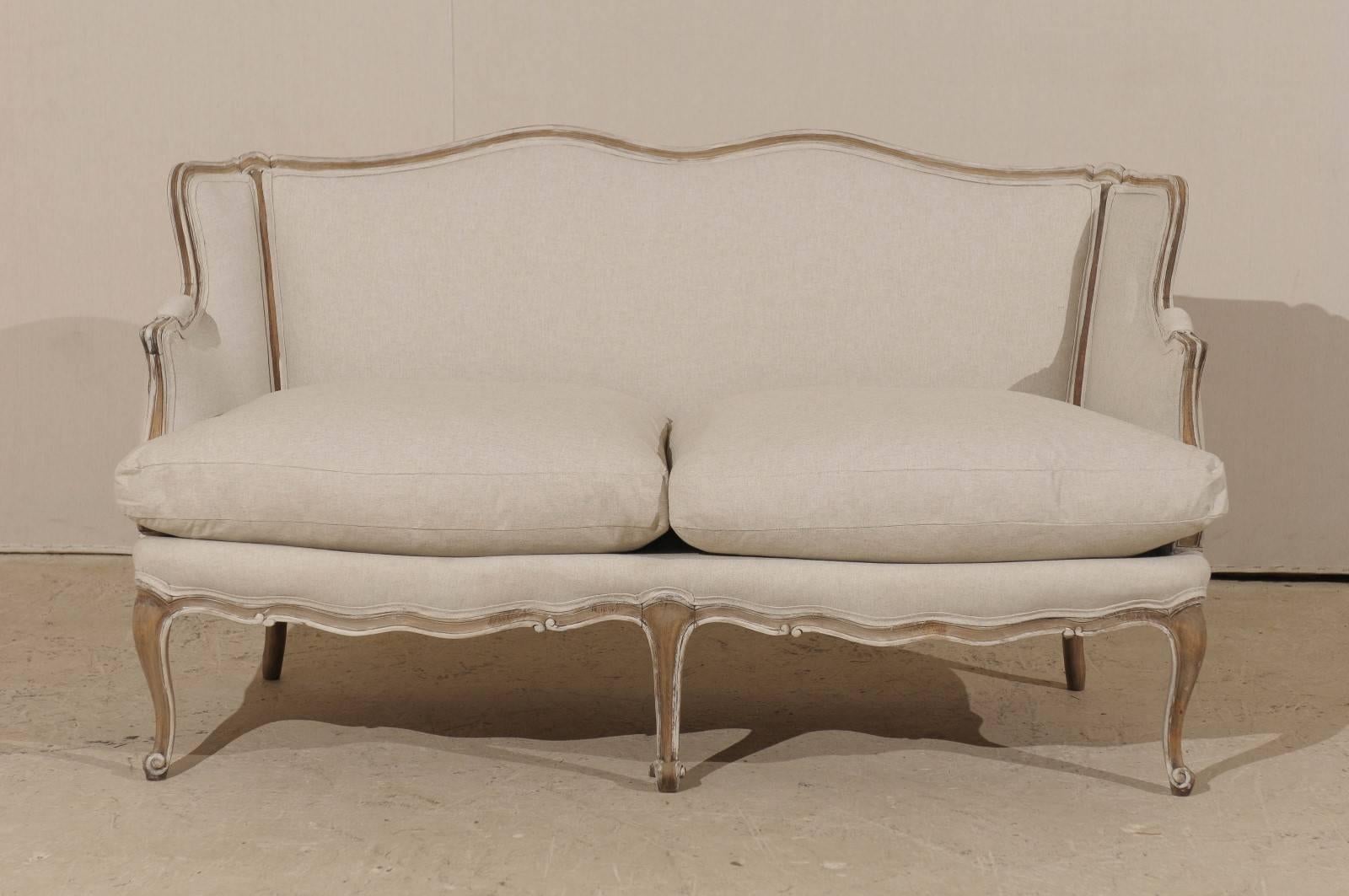A French Louis XV style painted wood sofa from the early 20th century. This French two-seat sofa features a scalloped skirt and cabriole legs resting on scrolled feet. The sofa's nicely curved wood frame with scrolled and partially upholstered arms