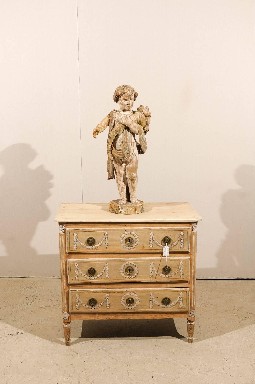 An Italian 18th century carved wood putto/cherub statue. This exquisite statue represents a putto figure in a walking stance, holding a cornucopia, symbol of abundance and prosperity. The figure, raised on a round base, is also adorned with a