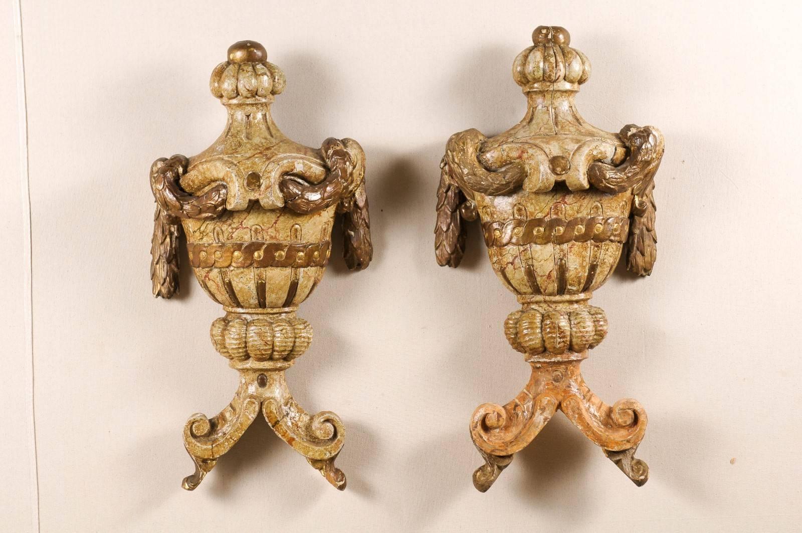 A pair of architectural ornaments. This pair of Italian wall hanging wooden fragments from the 19th century features two richly carved and marbleized urns decorated with swags on the lid and a guilloche frieze. In the lower part, the fragments are