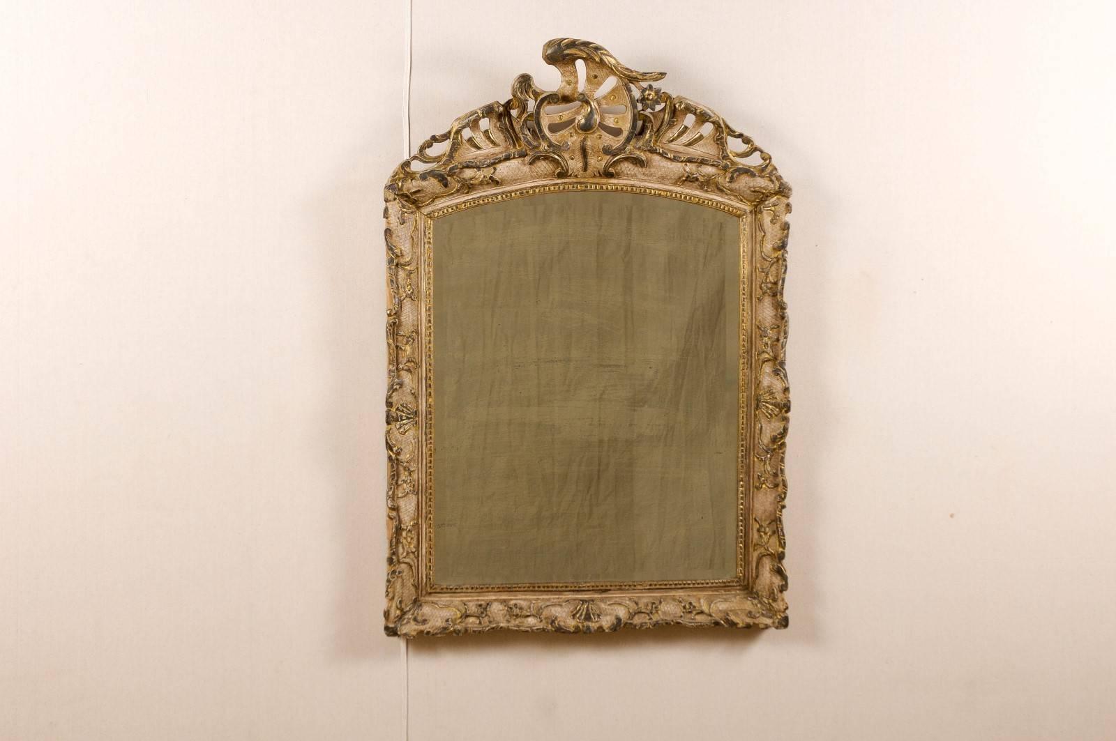 An Italian Rococo style painted and gilded wood mirror from the early 19th century. This Italian mirror features a grooved frame with a nicely carved crest, decorated with various scroll motifs and delicate flower. The frame is also adorned with a