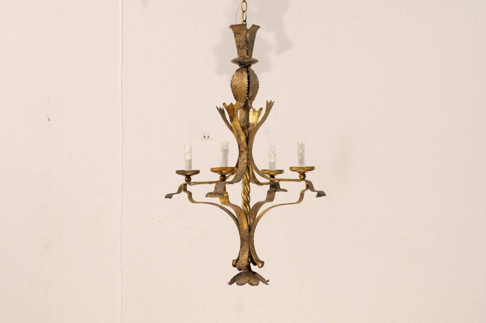 A French vintage four-light chandelier. This French chandelier from the mid-20th century is made of gilt iron. The twisted central column connects leaf motifs at the top to a floral motif finial at the bottom. This chandelier is a nicely aged gold