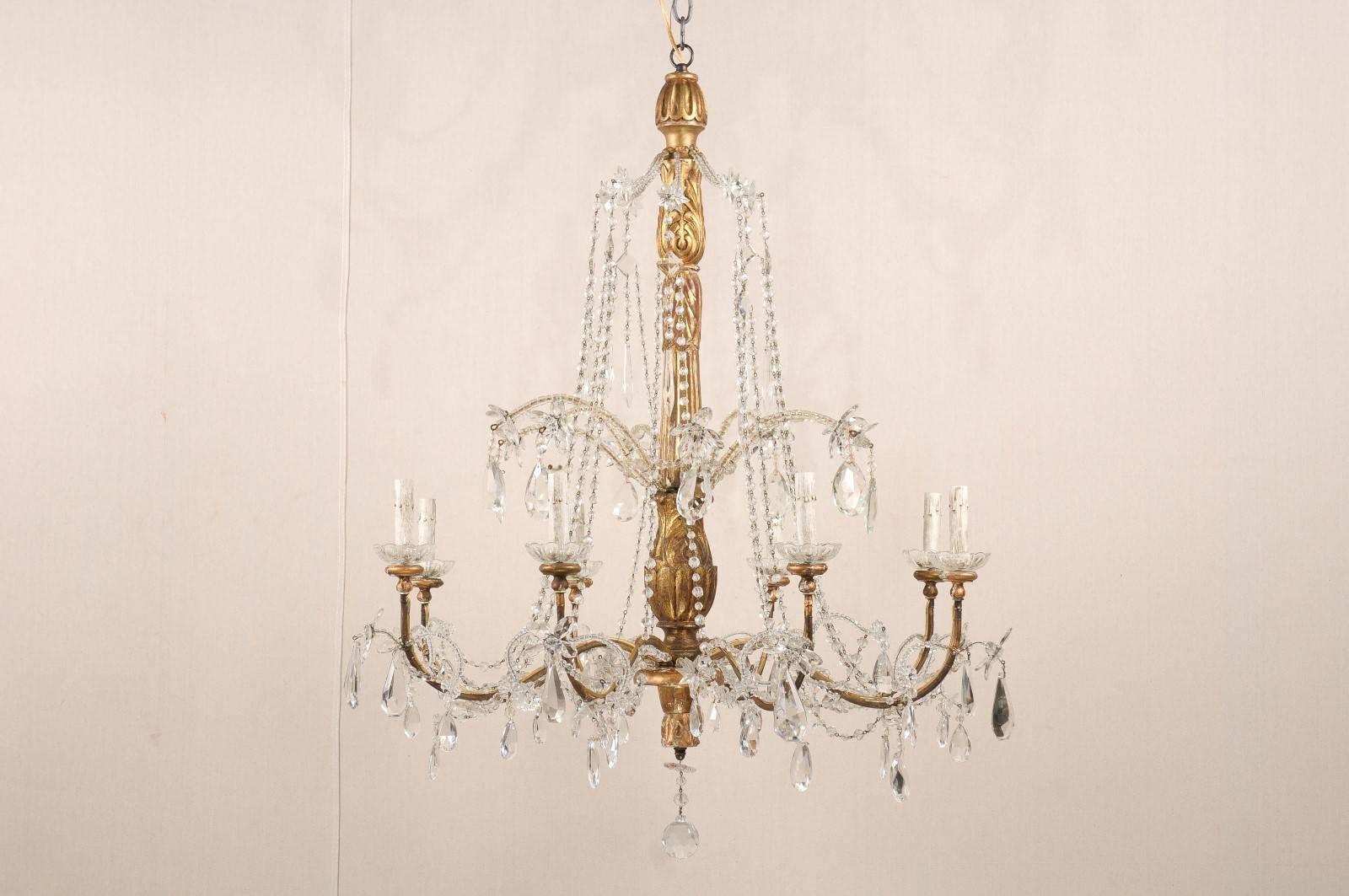 An Italian eight-light crystal chandelier with gilded wood central column from the 19th century. This Italian chandelier has eight scrolled arms stemming from a nice ornately carved central column and supporting the glass bobèches. Above the arms