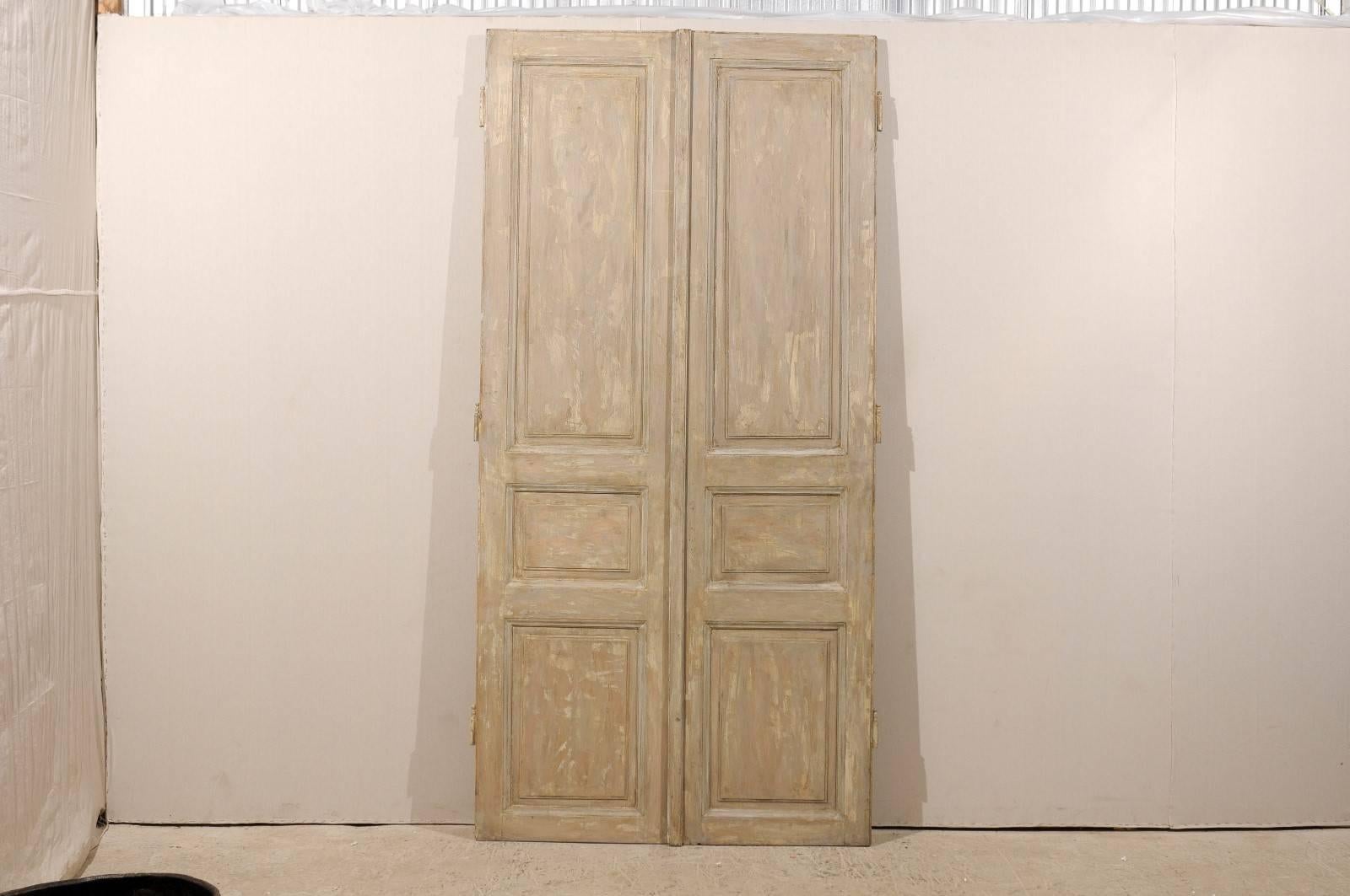 A pair of tall French doors from the mid-19th century. This pair of French wooden doors with carved panels features a brown color with traces of grey and cream accents. The trim around the carved panels is more of a light grey.  As with any of our