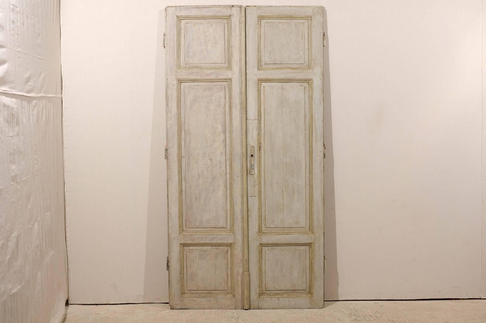 A pair of tall French doors from the mid-19th century. These French doors feature a grey green finish with wood coming through. They are made of three carved panels. They would be perfect on rails to separate rooms.