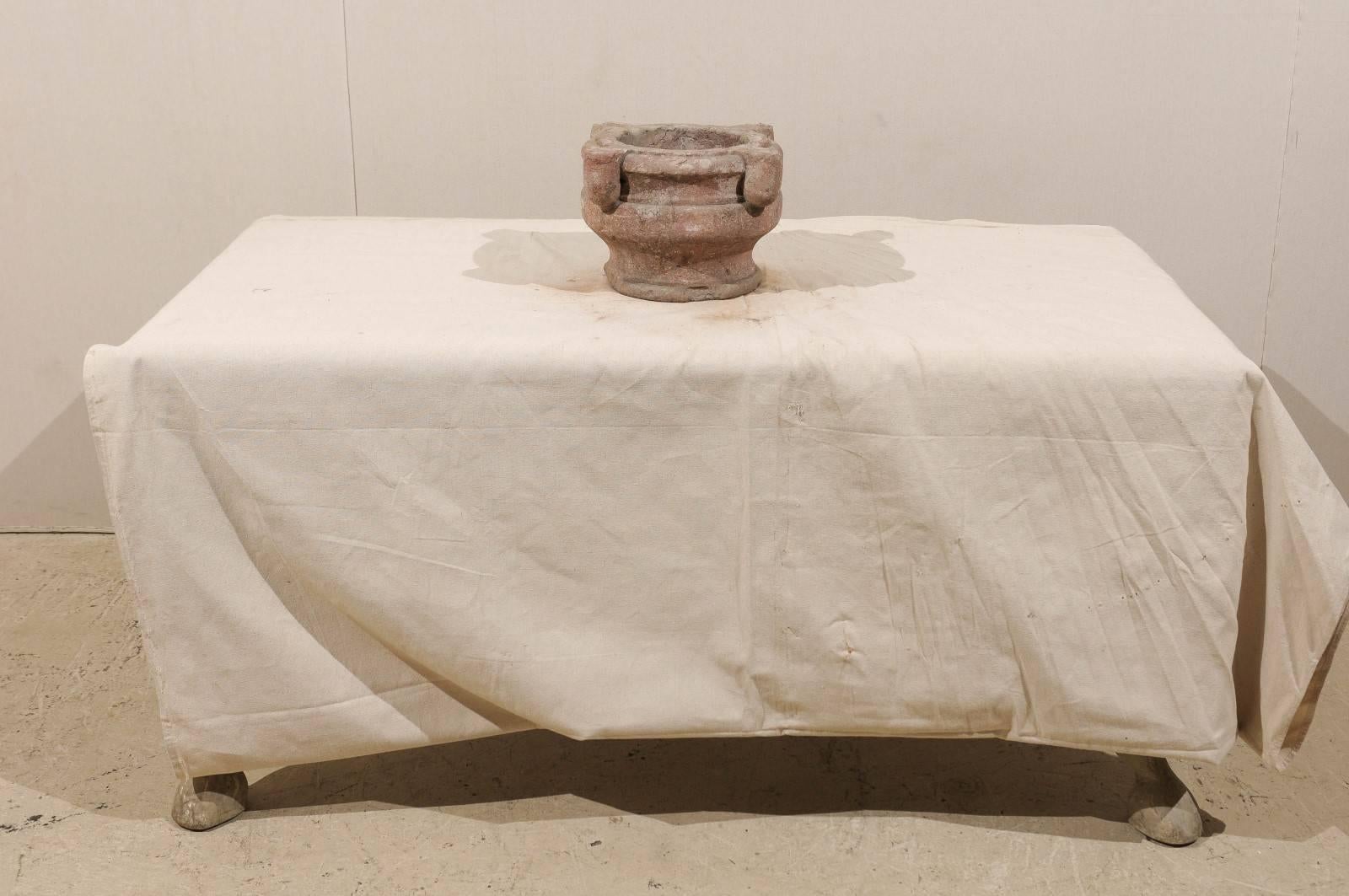 An Italian 18th century mortar. This antique mortar is adorned with four, three-dimensional decorations along the rim. The mortar is larger at the top, and swoops inward towards the base creating a curving look. The general tones are red with grey