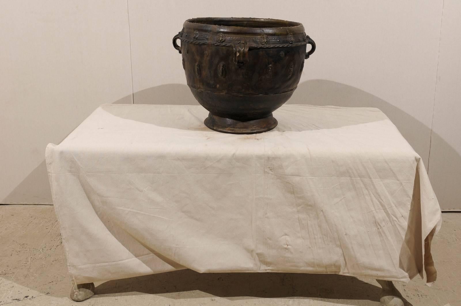 A Guatemalan jar made of clay with four handles. This clay jar has nice decorative motifs and roping details all around. The jar is of a deep brown-black color.