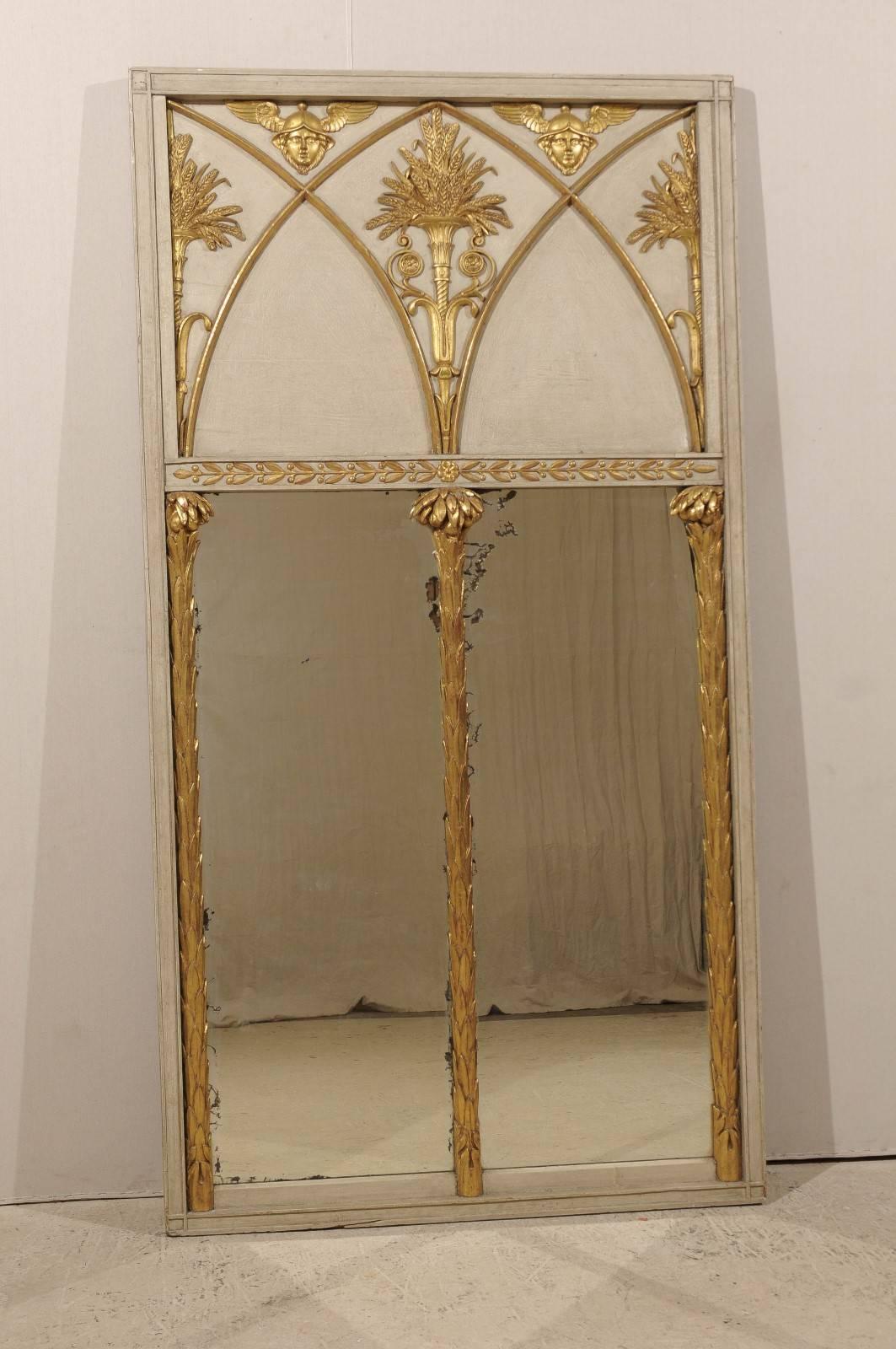 An English Regency period trumeau mirror. This 19th century wooden mirror features a painted frame highlighted with giltwood motifs inspired from the Greco-Roman vocabulary. The wooden panel in the upper part is divided by a decor reminiscent of