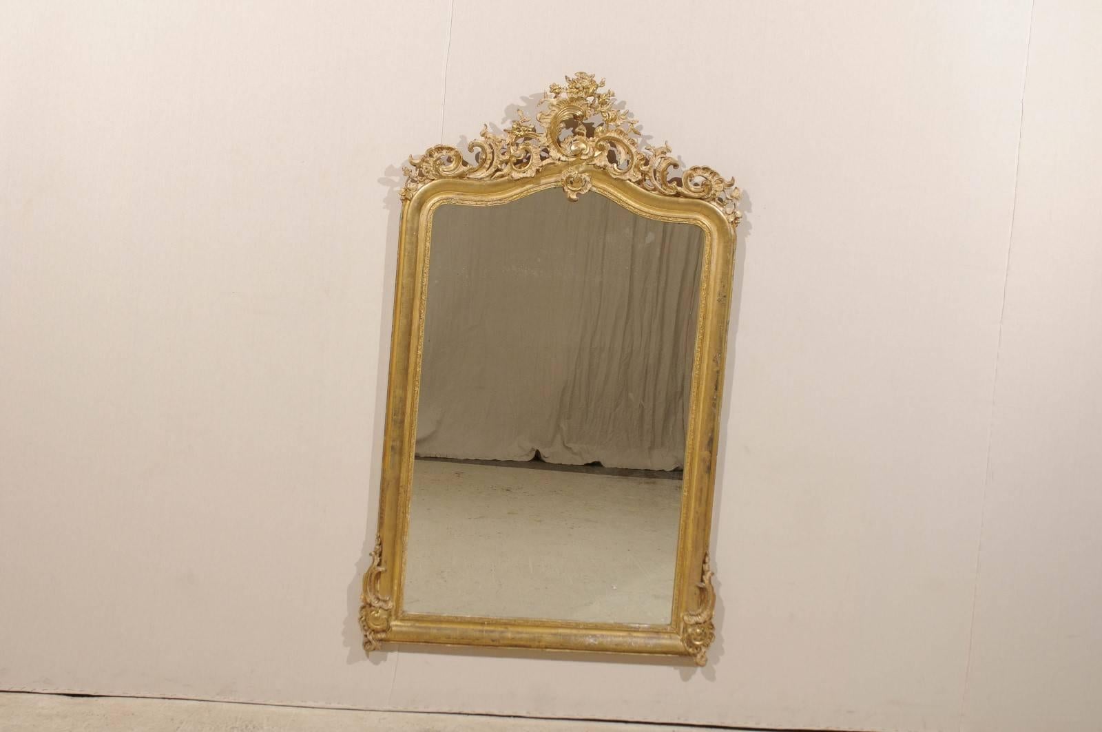 A French Rococo style wood carved mirror. This mid-19th century French giltwood rectangular mirror features a wonderfully carved crest and lower corner carved accents. The exquisite decor is made of asymmetrical 