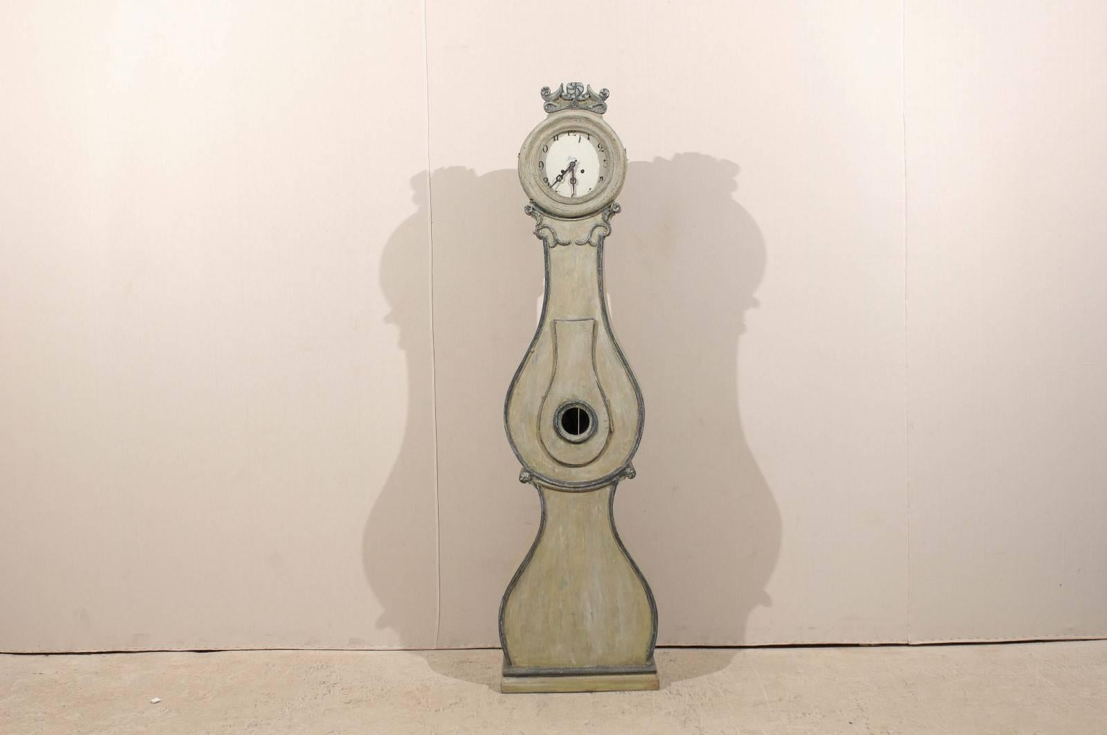 Une horloge suédoise du 19ème siècle avec des détails ornés. Cette horloge suédoise Fryksdahl de Värmland présente une crête joliment sculptée au sommet avec une rose et des rosettes stylisées. Le motif de la rosette est repris sur le col et la