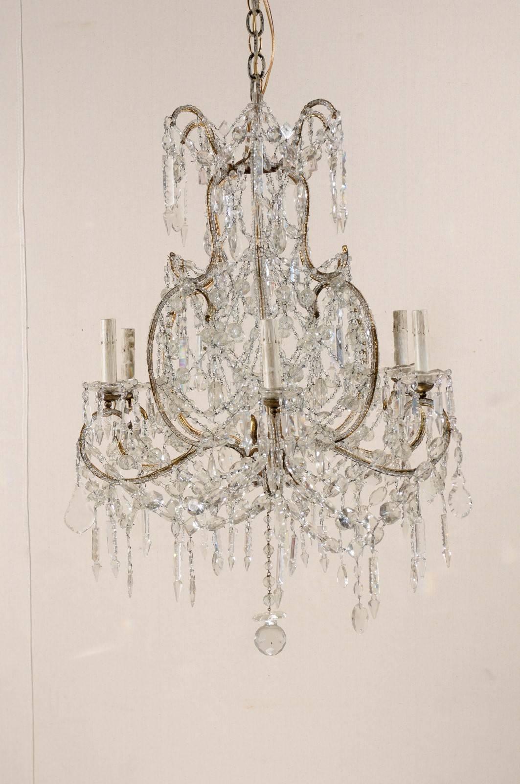A French, early 20th century crystal six-light chandelier with scroll arms. This crystal chandelier features a nice variety of shaped crystals. It is also adorned with a Classic round finial at the bottom. The various scrolls making the armature of