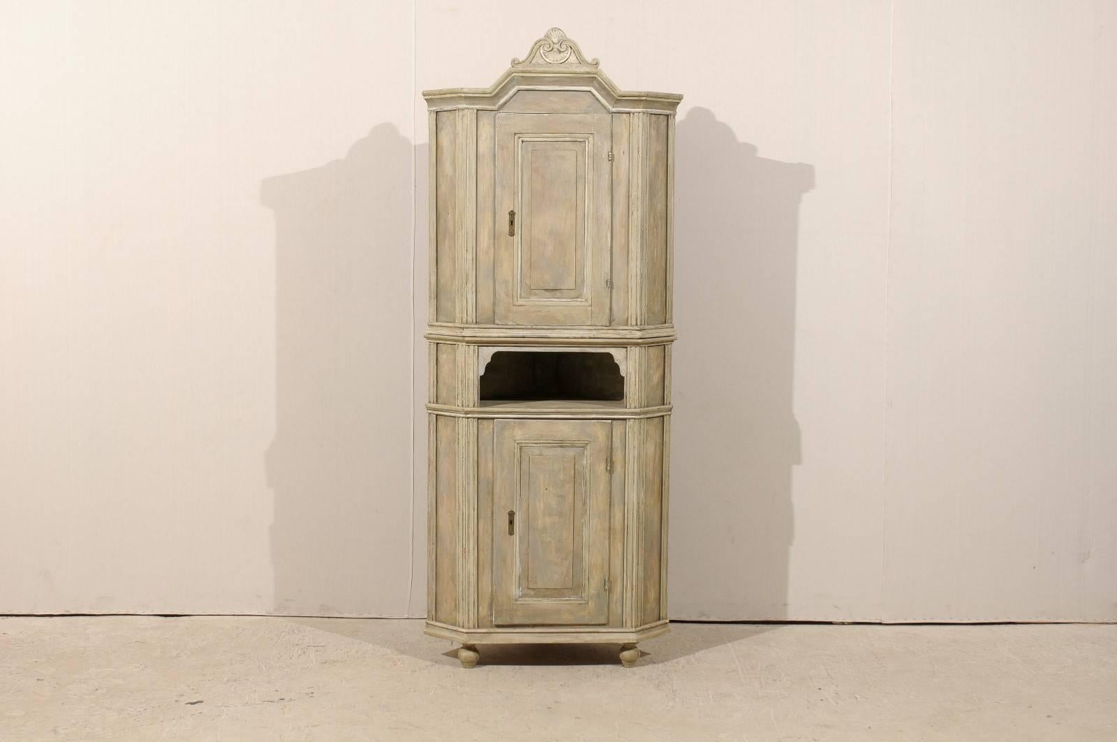 An early 19th century Swedish corner cabinet. This Swedish two-door cabinet, circa 1830, has a carved bonnet with shell and scroll motif on a carved pediment. This corner cabinet features a door at the top over an open shelf area and another door in