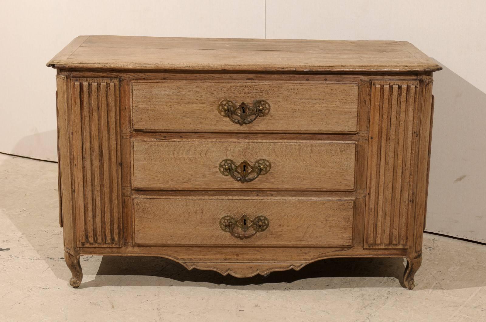 A wonderful French bleached-wood carved chest of drawers from the 18th century. This antique commode from France features three front drawers flanked within wide set, reed carved panels.  Each side panel of this chest has been fitted with a door for