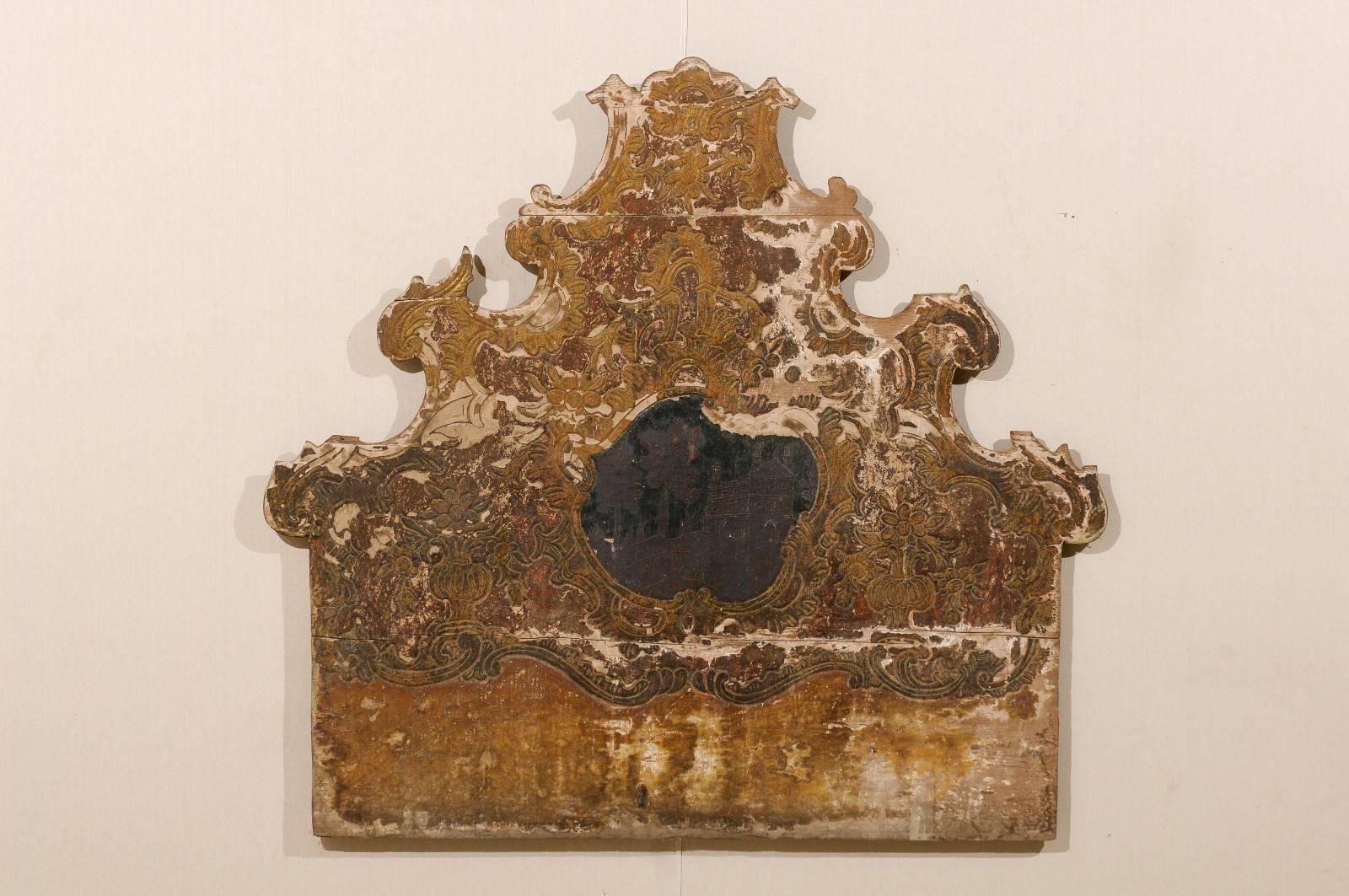 An ornately carved Spanish Rococo style wood headboard from the early 19th century. This headboard has its original paint which includes colors of a burnished red and warm yellow. There are traces of cream / brown color paint. The headboard is