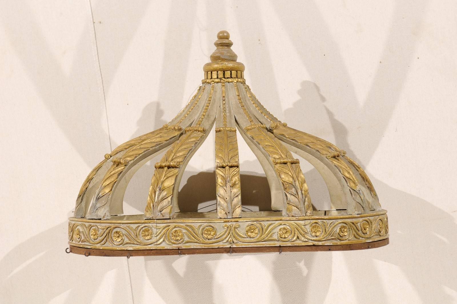 An Italian bed corona (bed crown). This early 20th century Italian wood bed corona is a nice grey-light green color accented in gold gilt and features floral and stylized acanthus carvings over a Rinceaux frieze. This piece could be hung above a bed