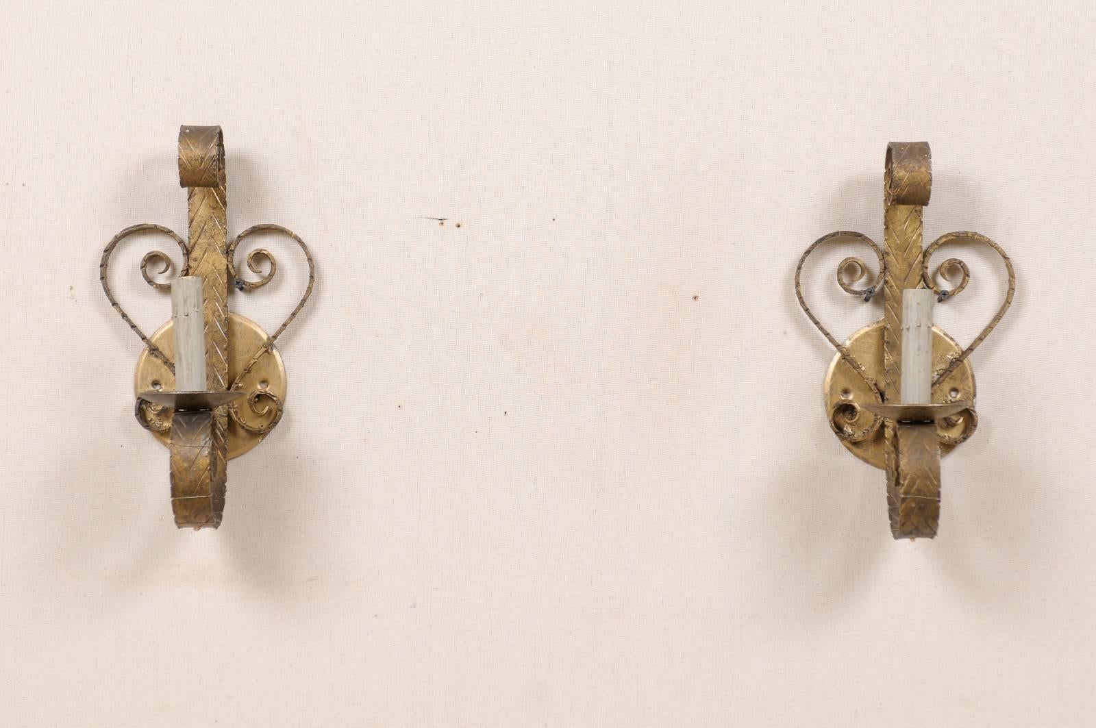 A pair of Spanish painted gold forged iron single light sconces from the mid-20th century. Each sconce features a central scroll attached to the backplate. Each sconce is also decorated with S-scroll motifs on either side creating a heart shaped