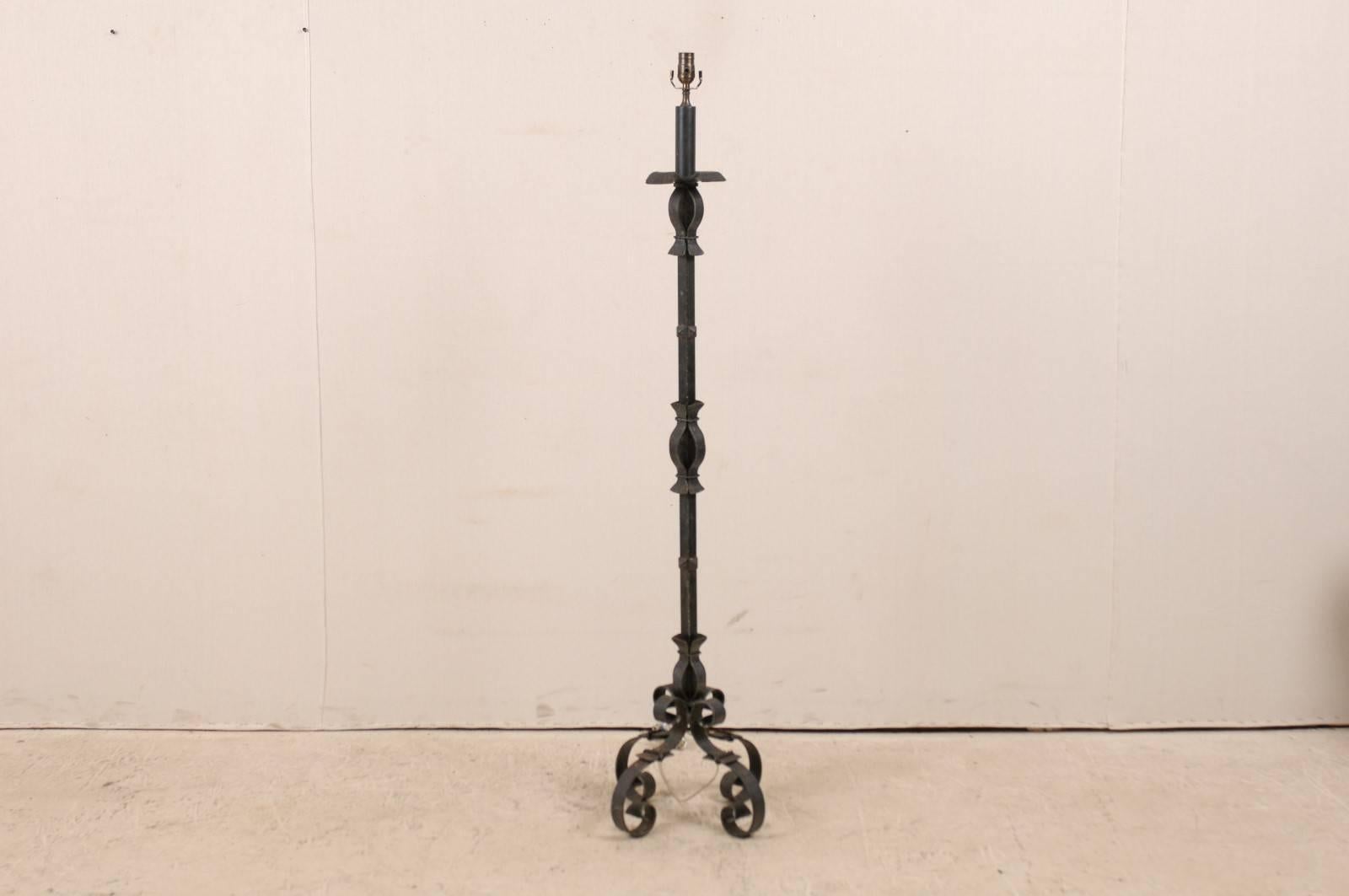 A French sleek black colored forged iron floor lamp from the mid-20th century. This floor lamp rests on four scrolled feet. This tall lamp is black in color with some warm rust accents throughout. It has been rewired for the US.