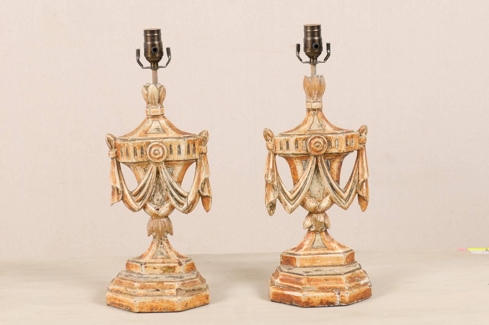 A pair of Italian painted and carved wood table lamps from the early 20th century. This pair of table lamps features its original paint and is adorned with urn and swag carvings. The primary color of this pair is orange and cream with a little brown