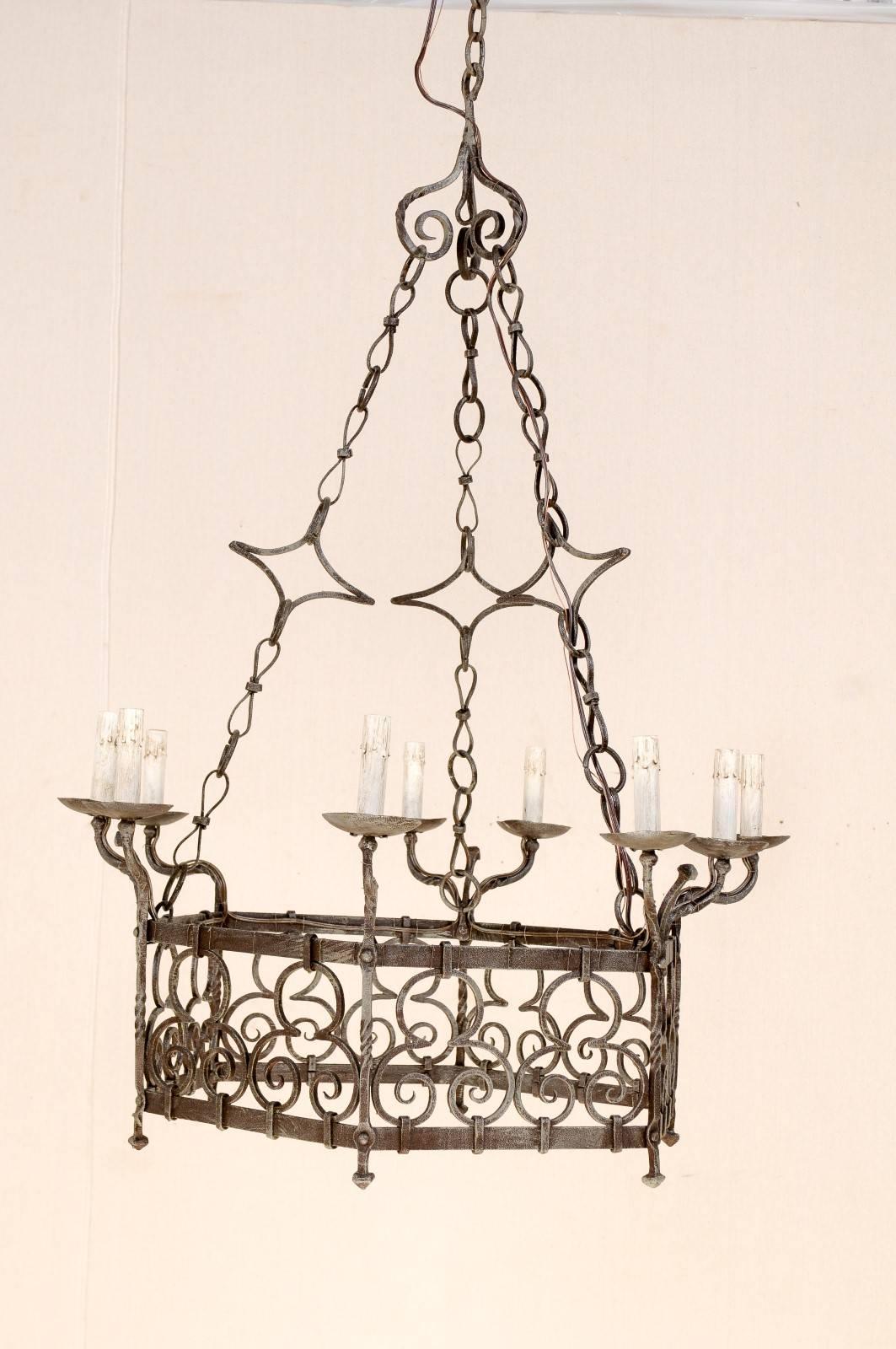 A French Gothic style nine-light iron vintage chandelier. This French chandelier from the mid-20th century has a hexagonal ring with scrolled designs. The lights are rotated in single and then double posts that curve up and away from the centre. The
