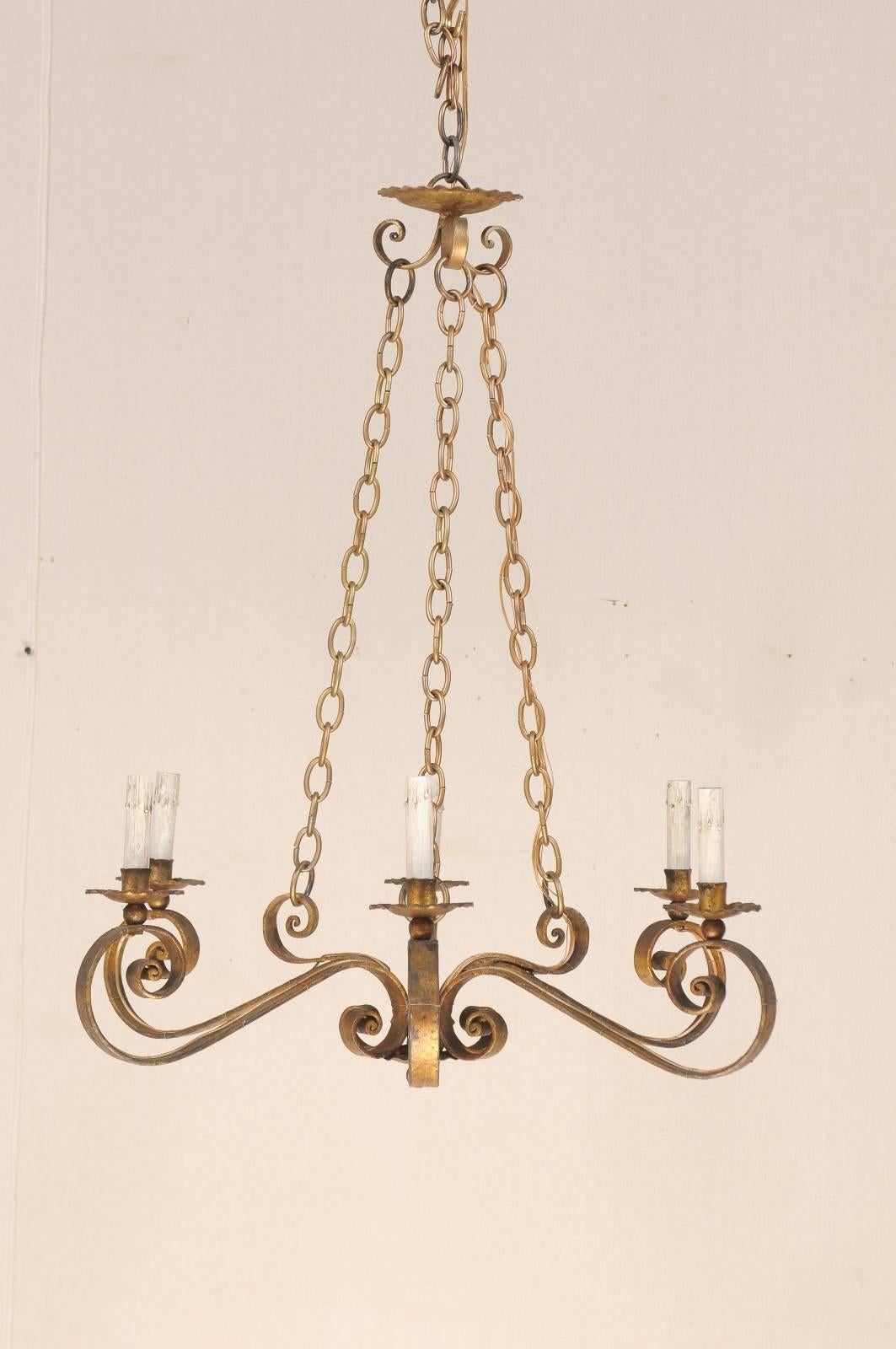 A Spanish 19th century gilded iron six-light chandelier. This Spanish chandelier from the mid-19th century features six scrolled arms connected at centre that span out to create a circular shape and support the bobèches and painted candle sleeves.