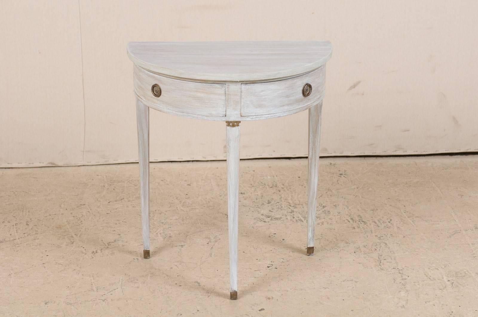 A Swedish petite demilune style table. This cute little Swedish table from the mid-20th century has two drawers and three tapered legs. This piece also features clean lines and is painted in a pale blue wash.