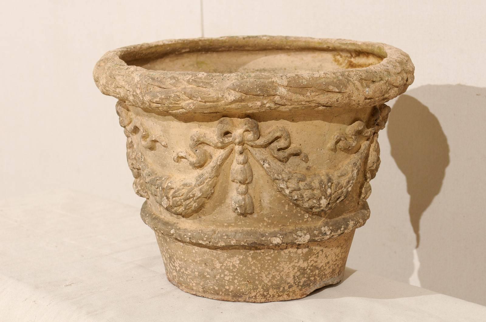 A French terracotta garden pot. This French pot from the 20th century has a subtle conical shape and is adorned with a repeating bow and swag motif. This pot has an overall beige-cream color. There is really nice patina and age throughout. This