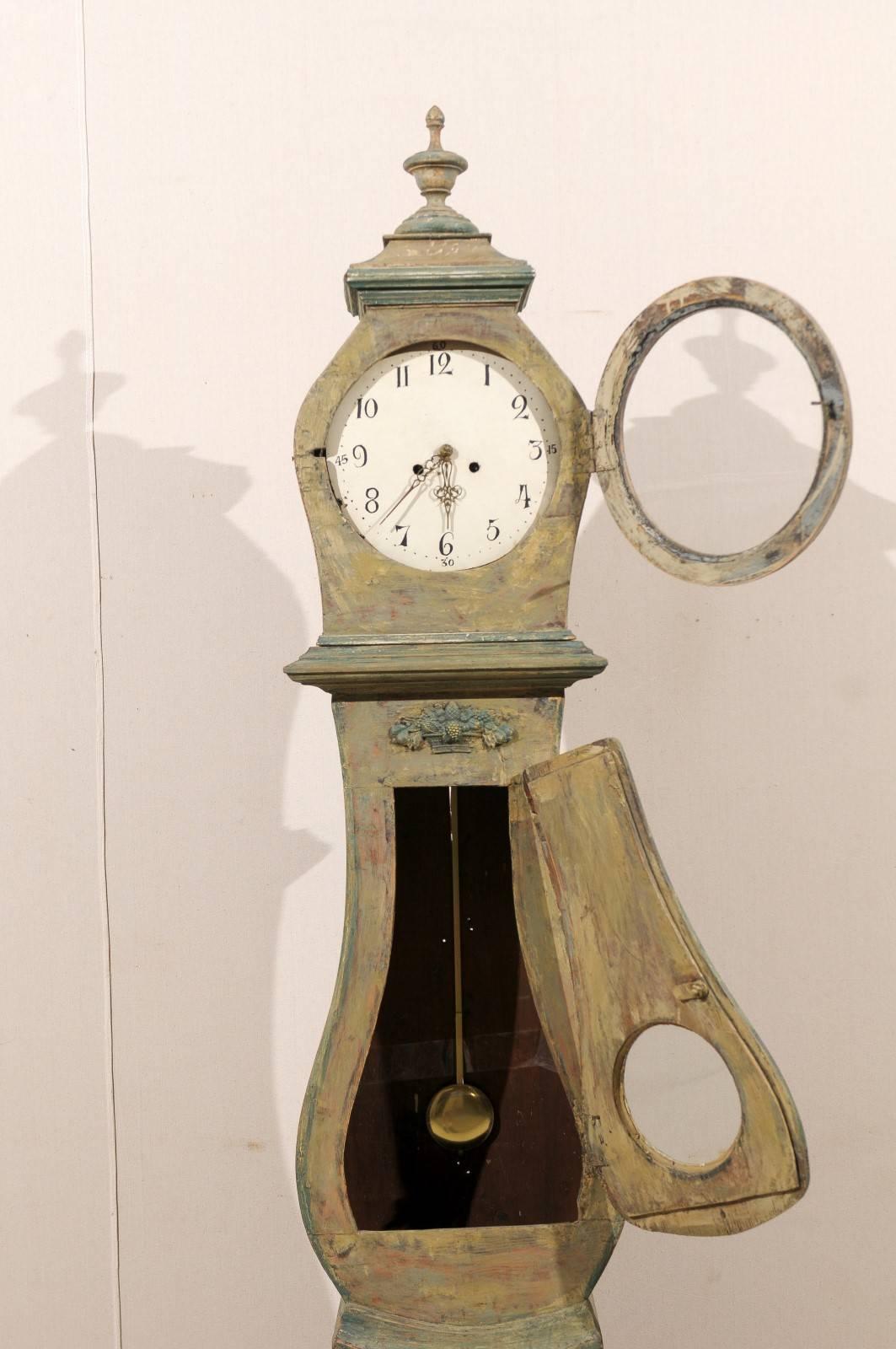 Une horloge suédoise du 19ème siècle. Cette horloge en bois peint présente un cimier joliment sculpté avec une urne en son centre. Le col est décoré d'un motif exquis de panier de fruits en son centre. Cette horloge a conservé sa face métallique,