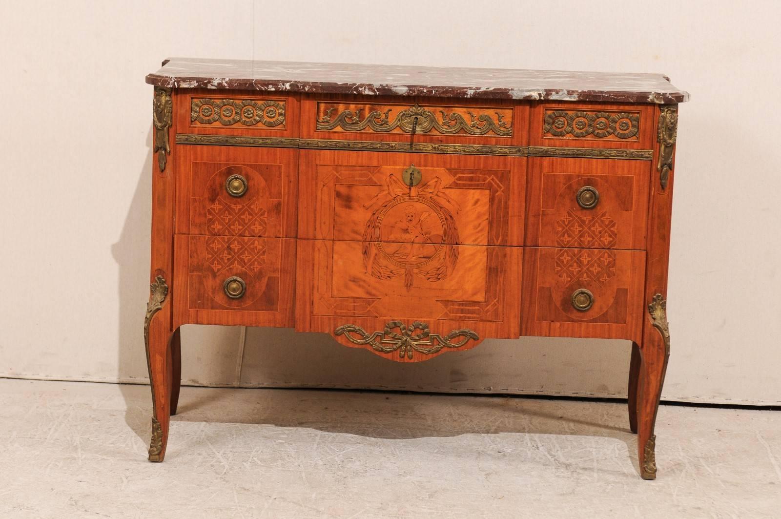 A Swedish mid 20th century Gustavian style three-drawer chest with marble top. This 1940s Swedish chest features exceptional inlay details featuring a flute playing Putto centered within a wreath and a bow at it's top. The chest sides each have a