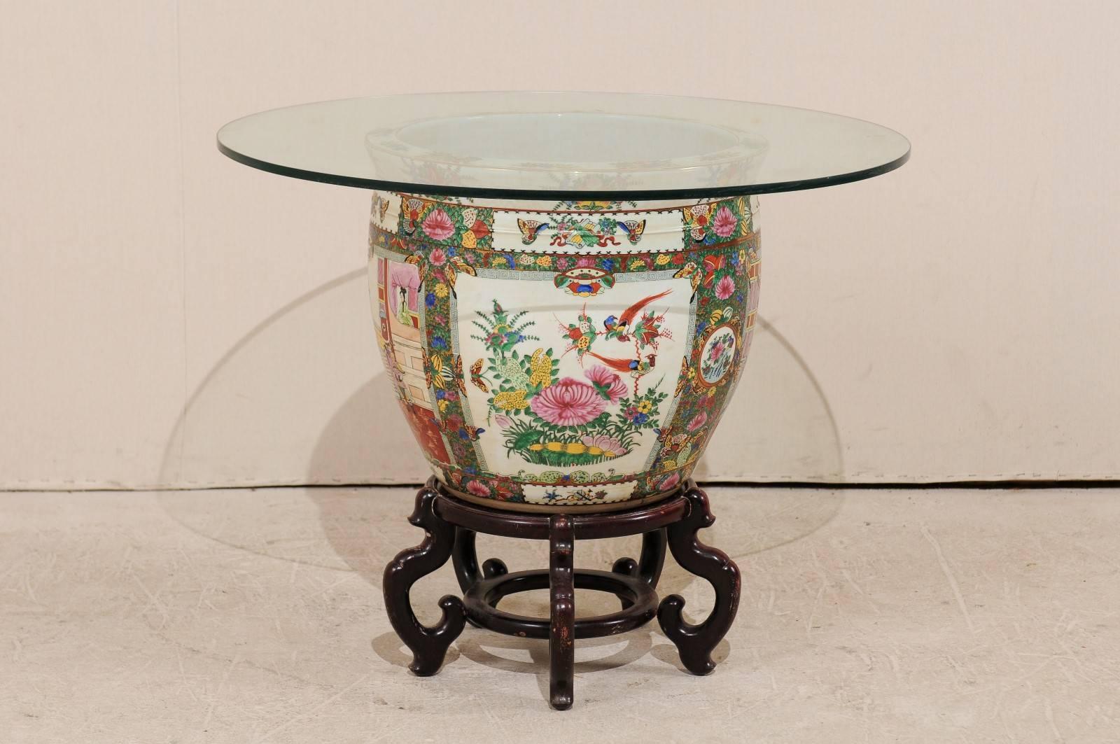 A Chinese Famille rose base and glass top table. This round-shaped Chinese table features a glass top over a large Famille rose porcelain vase. There are beautiful depictions of birds and flowers about the outside of the base with koi and aquatic
