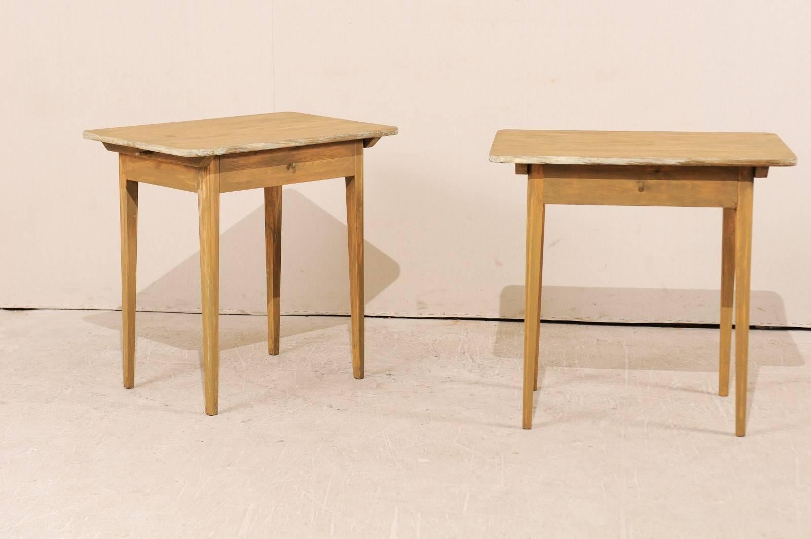 A pair of Swedish early 20th century single drawer tables. This pair of Swedish side tables each feature a single drawer, and have a simple yet elegant structure, with long slightly tapering legs. These tables have a light wash of warm beige with