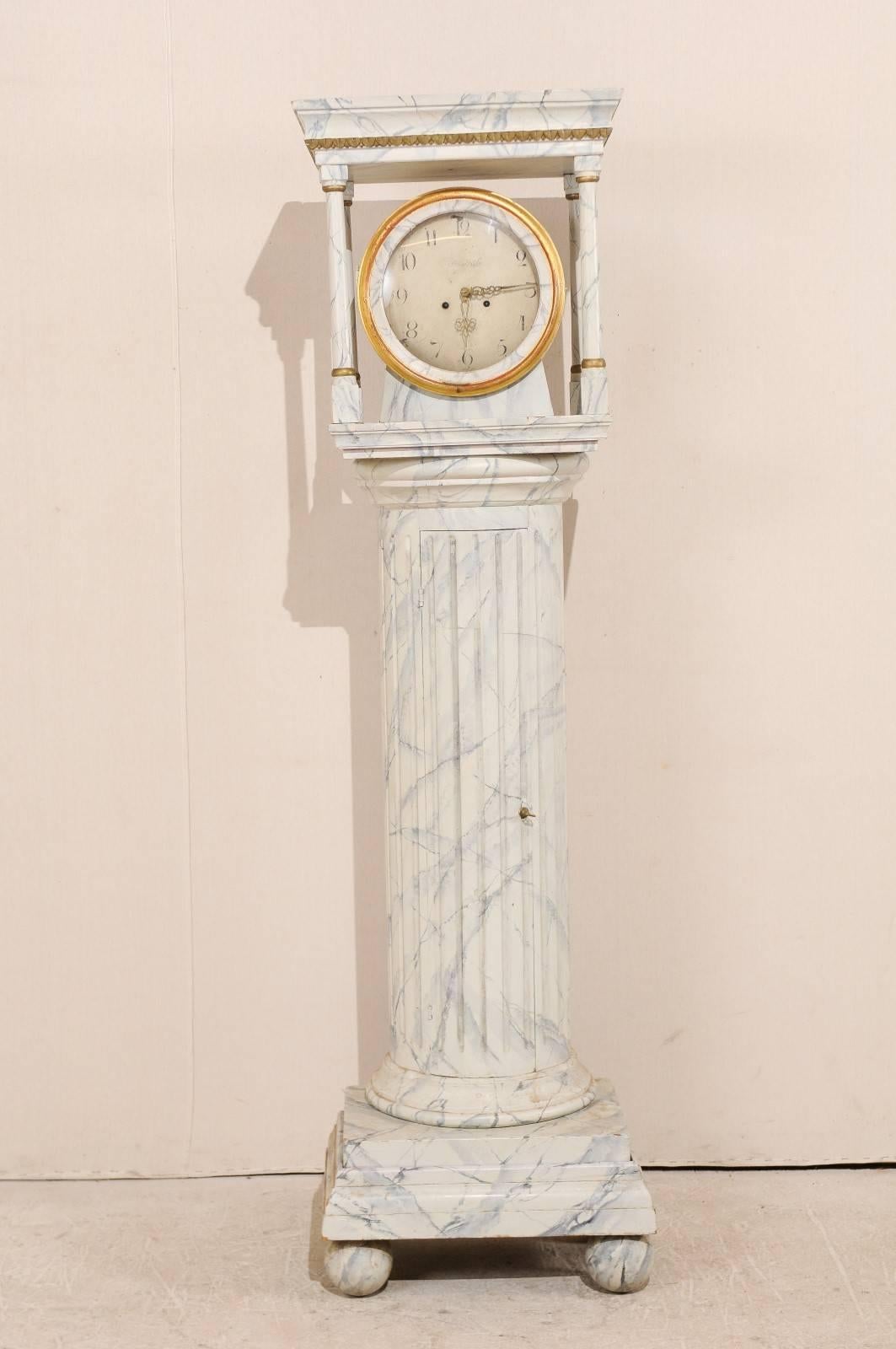 A Swedish 19th century long case clock. This Swedish floor clock, circa 1820s, features a semi-circular column body with vertical fluting and faux marbling throughout. This clock retains it's original metal face, hands and movement. The head, with