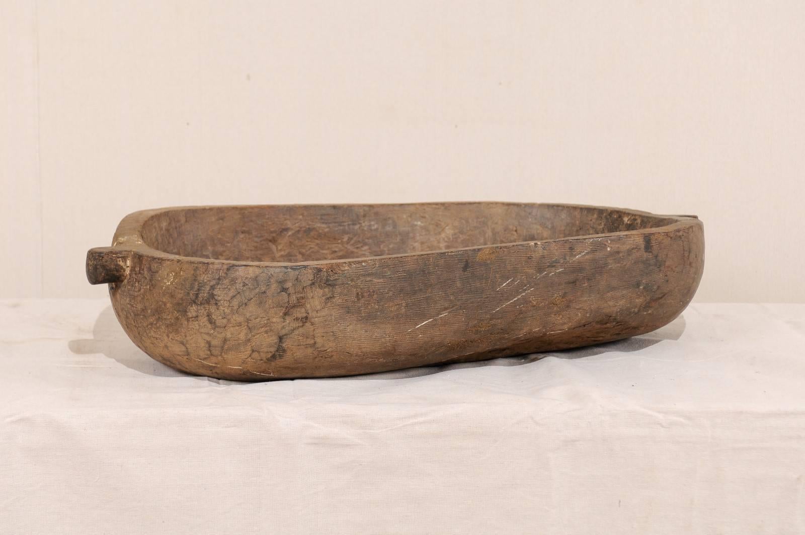 A vintage Naga carved wood bowl. This beautifully Primitive bowl has been carved from a single piece of wood, features and oblong shape and a single handle at either end. These bowls were originally used in kitchens of the Naga people for various