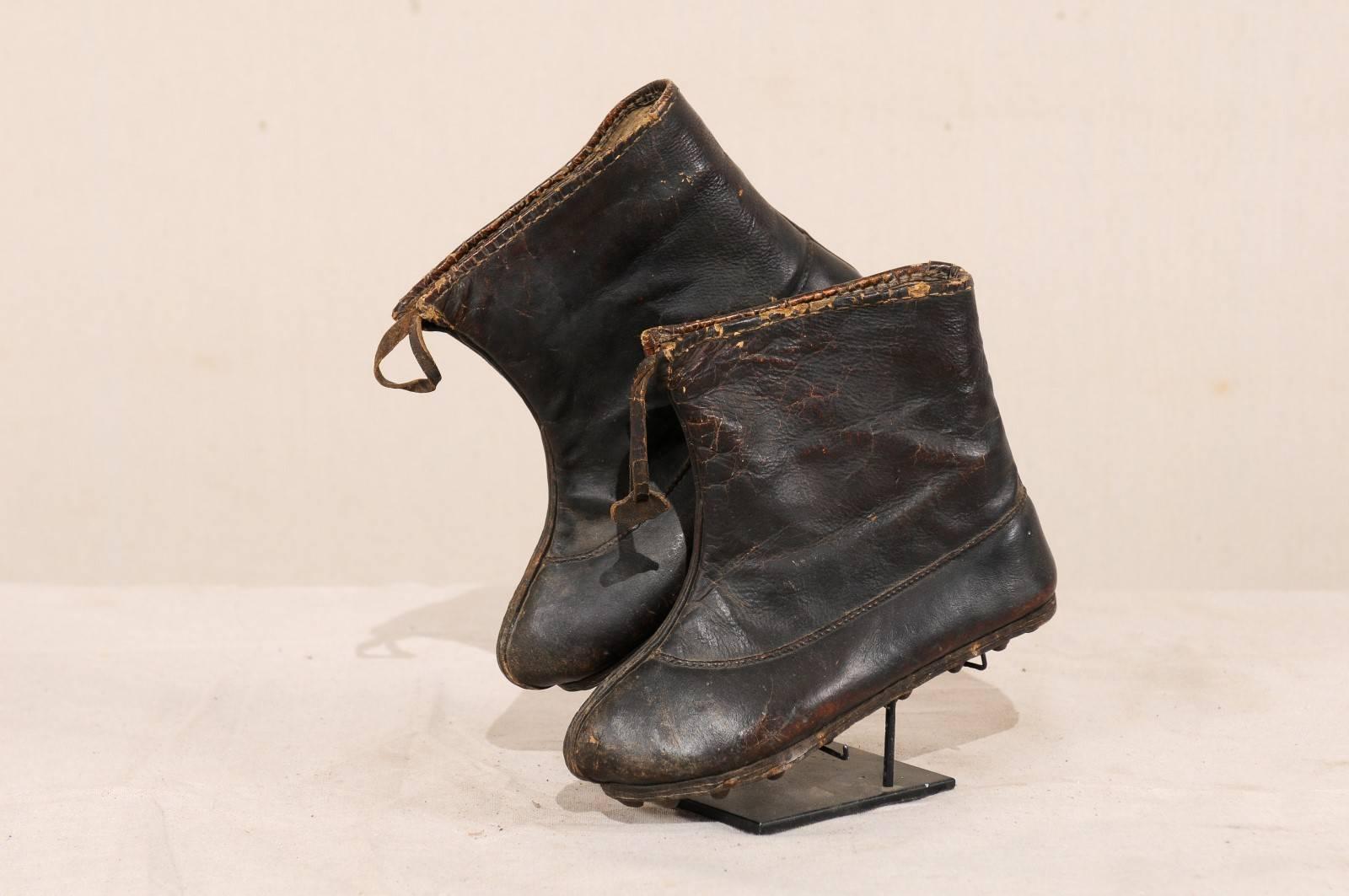 A pair of vintage Chinese winter boots on stand. This is a pair of Chinese leather winter boots that have been displayed on a custom black iron Stand. The boots are from the people belonging to the South West tribal regions of China. These boots