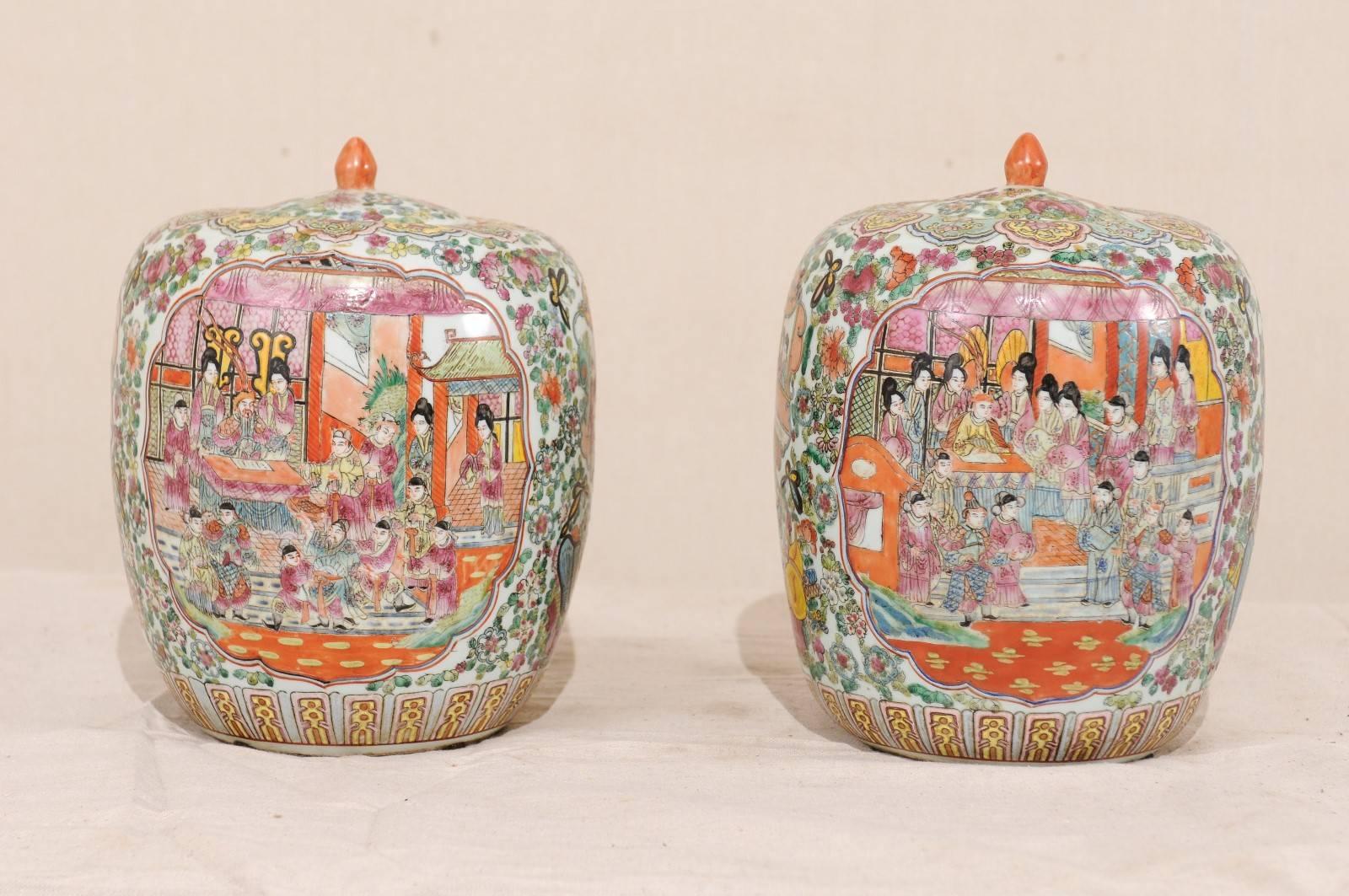 A pair of Chinese Famille Rose porcelain lidded jars from the mid-20th century. This pair of Chinese porcelain jars with lids have a bulbous form, decorated in the typical Famille Rose palette. The body of the vases are decorated with two large