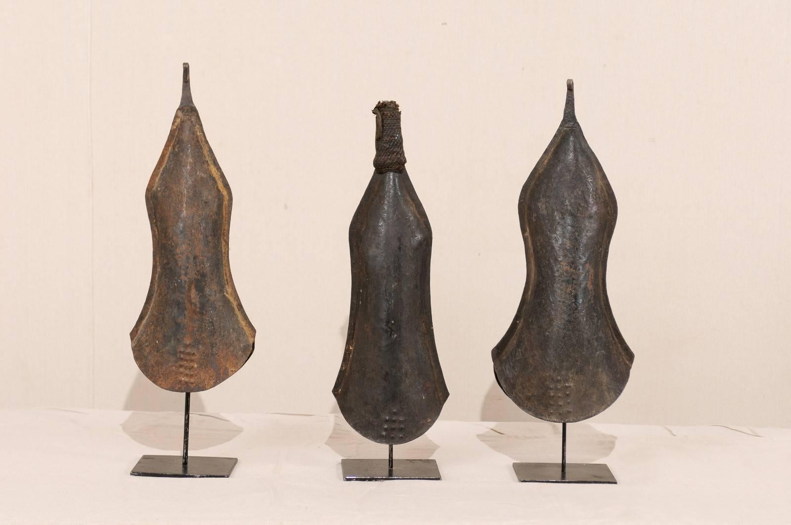 A collection of African hand-forged iron bell currency on custom stands from the 20th century. This is a collection of three African bell currencies of hand-forged iron on custom black iron stands. These bells were made by the tribal blacksmiths of
