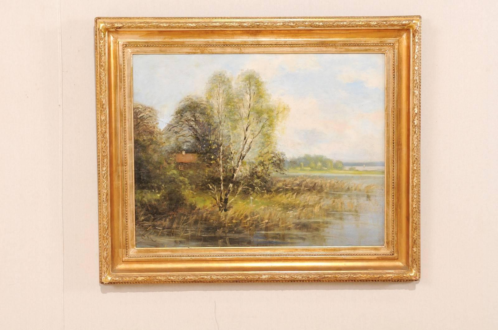 A Swedish landscape oil painting in frame. This is a lovely painting depicts a homestead and surrounding landscape by the water. This painting is within a gold wood carved frame. Signed 