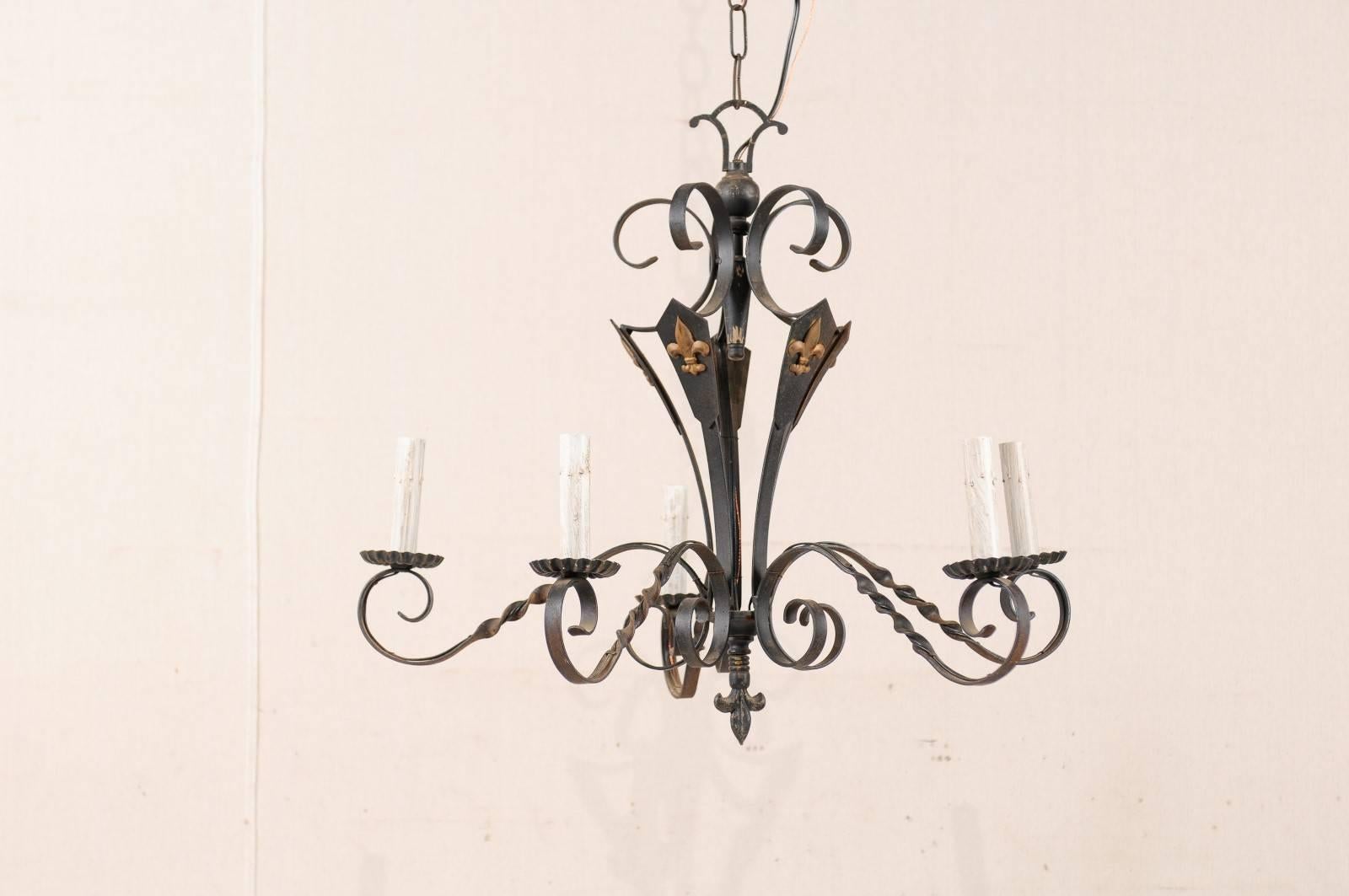 A French five-light dark colored iron chandelier with painted gold accents. This French vintage mid-20th century chandelier features five s-scrolled and twisted arms which each support the metal bobeches and painted candle sleeves. The central body