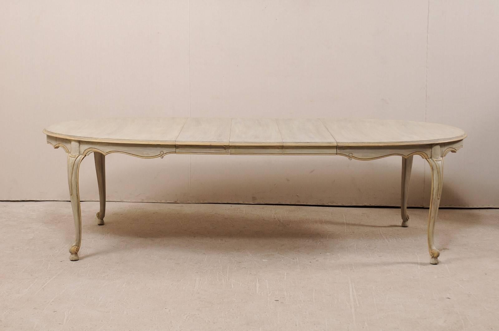 An American mid-20th century oval dining table. This dining painted wood dining table features a nicely carved and outlined skirt and is raised on four cabriole legs with scrolling details at their feet. The table has three leaves which allows for