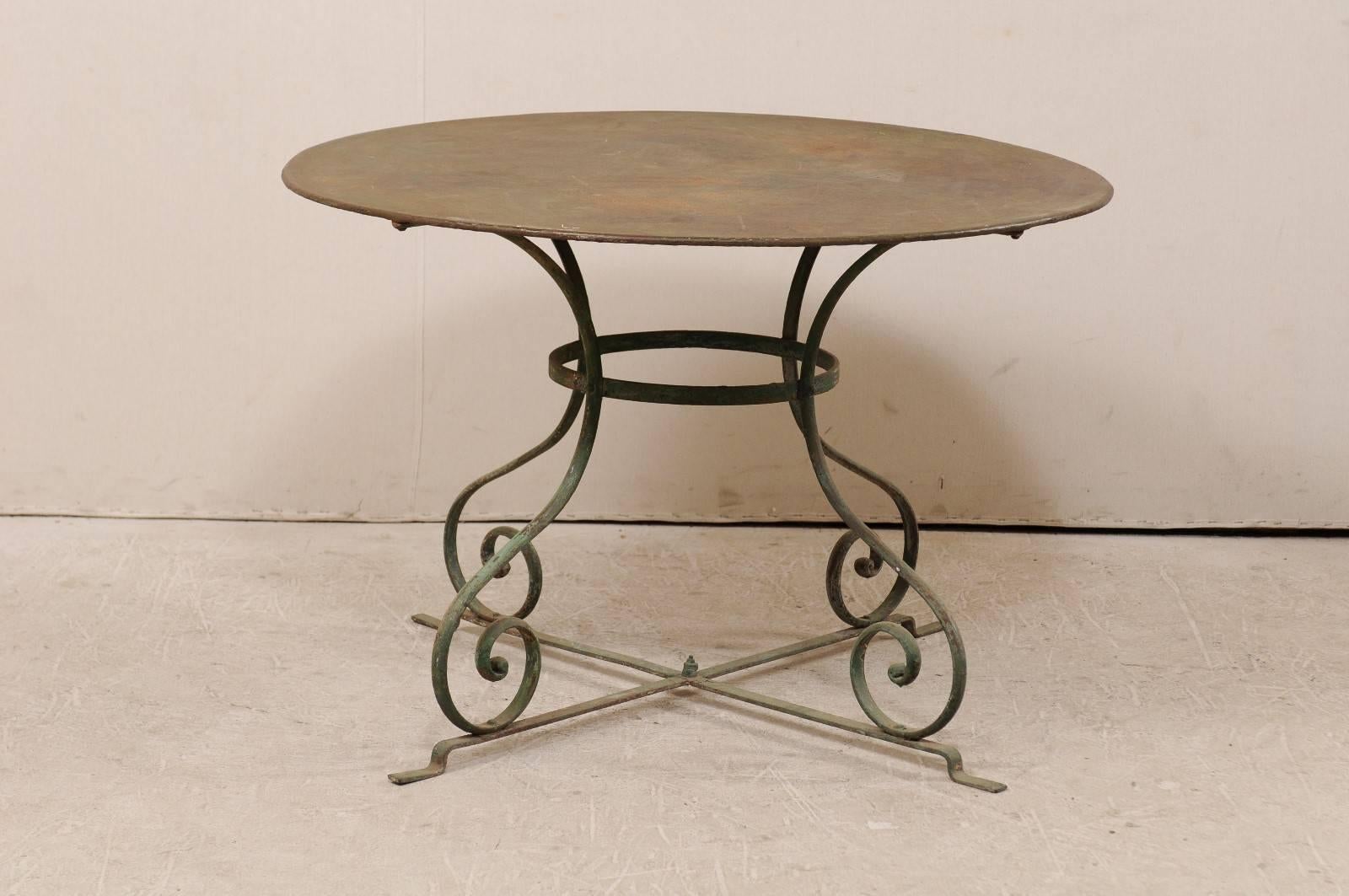 A French mid-20th century patio dining table. This round shaped metal patio table has a wonderfully aged patina and features a round top over four scrolling legs. Each of the four legs are connected to a circular center and bottom cross bar for
