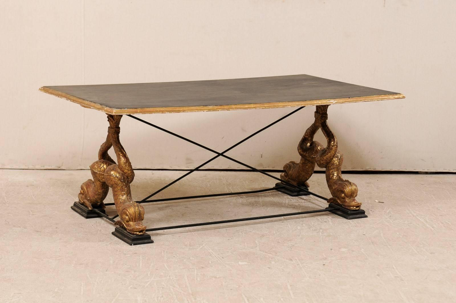An Italian mid-20th century coffee table. This coffee table features a painted wood top which is held up by carved wood mythological fish. These mythological creatures have long, twisted and richly scaled bodies, the tips of the tails join together