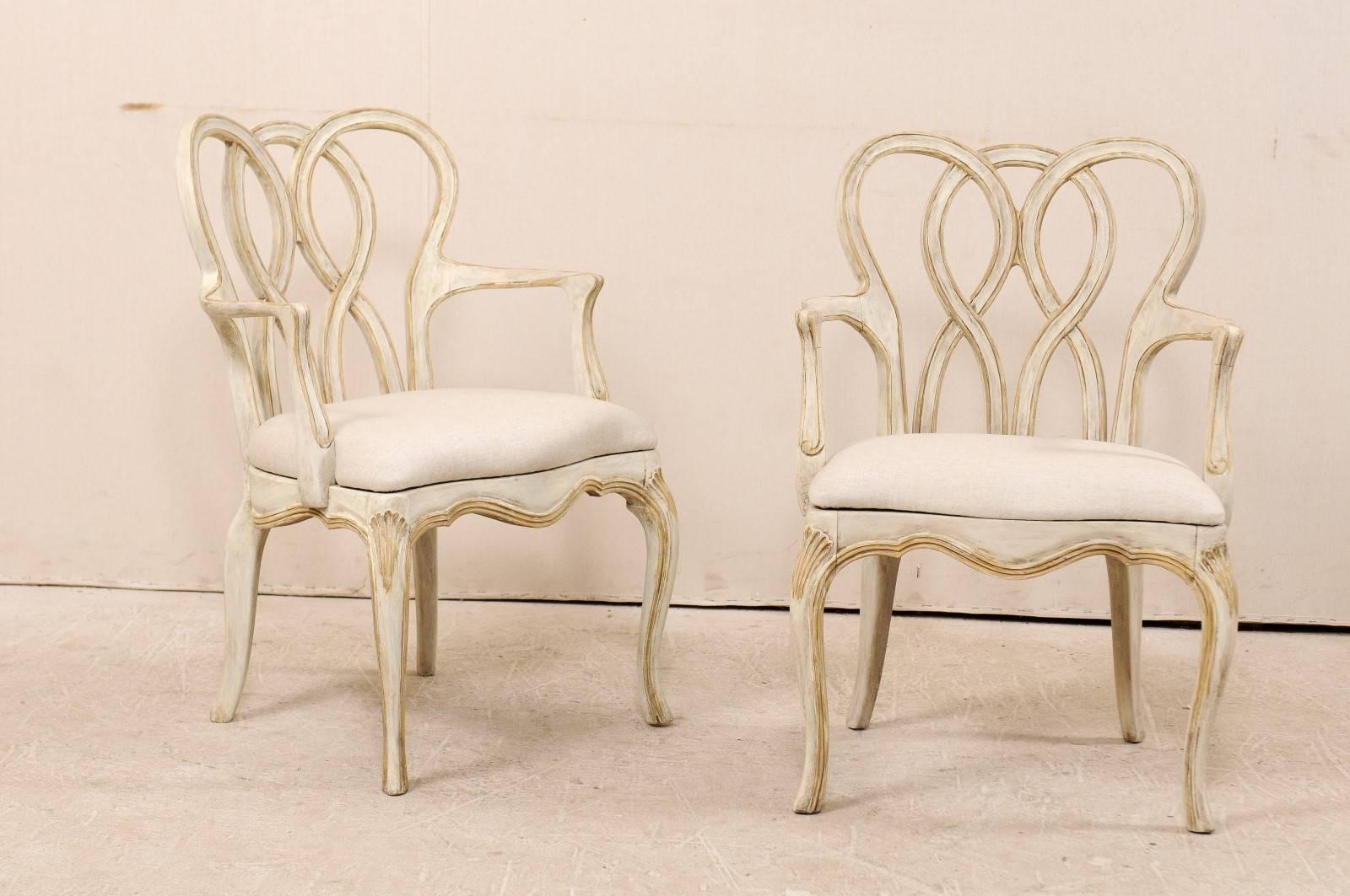 A pair of American made Italian Venetian style painted wood chairs. This Mid-Century pair of armchairs feature triple intertwined back-splats and beautifully scalloped skirts. The chairs are raised upon cabriole legs with carved shells at their