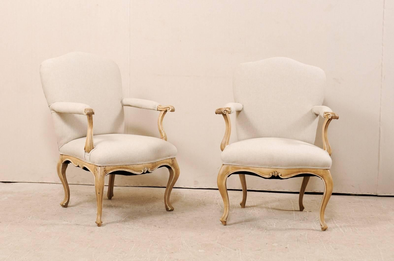 A pair of Italian 19th century carved wood and upholstered armchairs. These Italian arm chairs feature camel shaped backs, nicely carved skirt, arms and legs. There is a carved scroll motif about the knuckles which terminate into the upholstered are