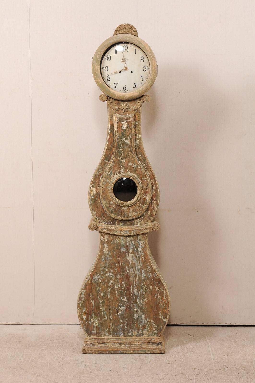 A 19th century, Swedish painted wood Fryksdahl clock. This Fryksdahl clock features a carved crest depicting some foliage with a central flower, volute accents at the neck with a central star, an accentuated waist, and round face. This clock retains