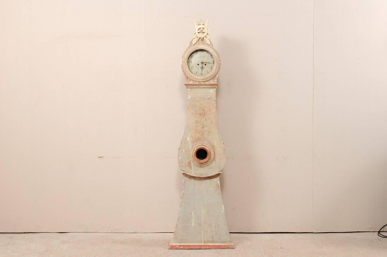 An 1820s Swedish painted wood clock. This Swedish clock from Norrbotten County, Sweden (Northern region) features a handsomely carved exaggerated crest, a circular face and neck is accented with additional trim. This clock retains it's original