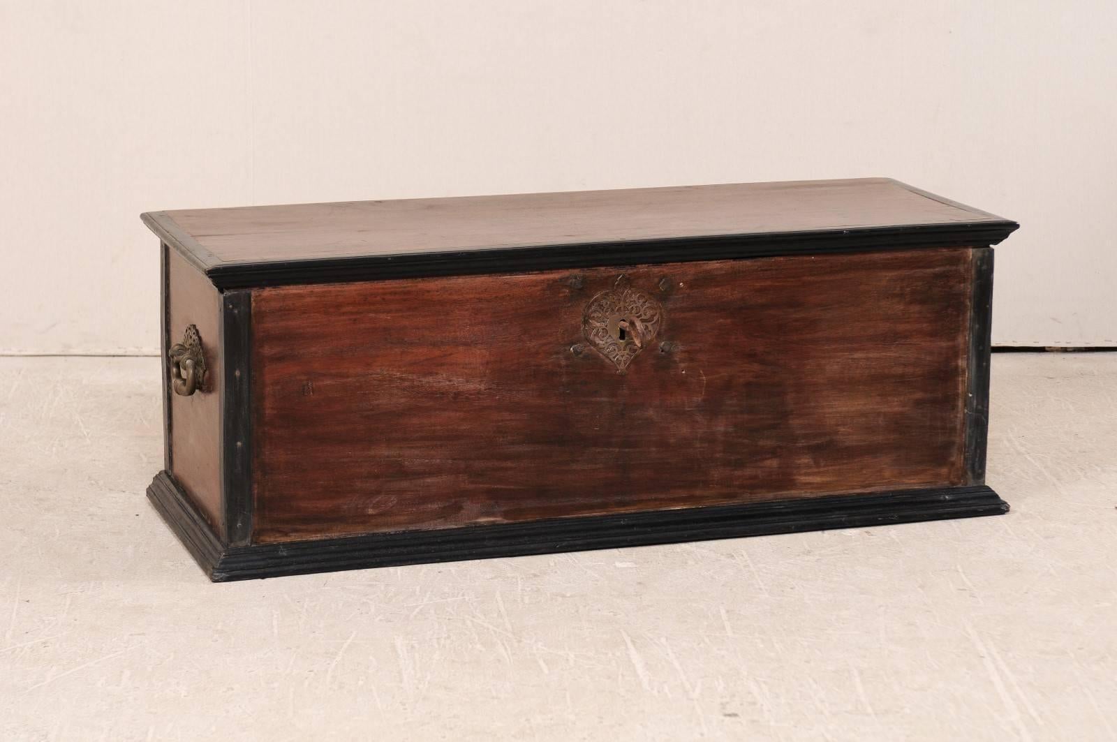 An early 20th century large size wood coffer. This Indian trunk from the early 20th century has a rich wood tone, and is accented with black along the top and bottom trims, as well as each corner post. This coffer is adorn with nicely sized handles