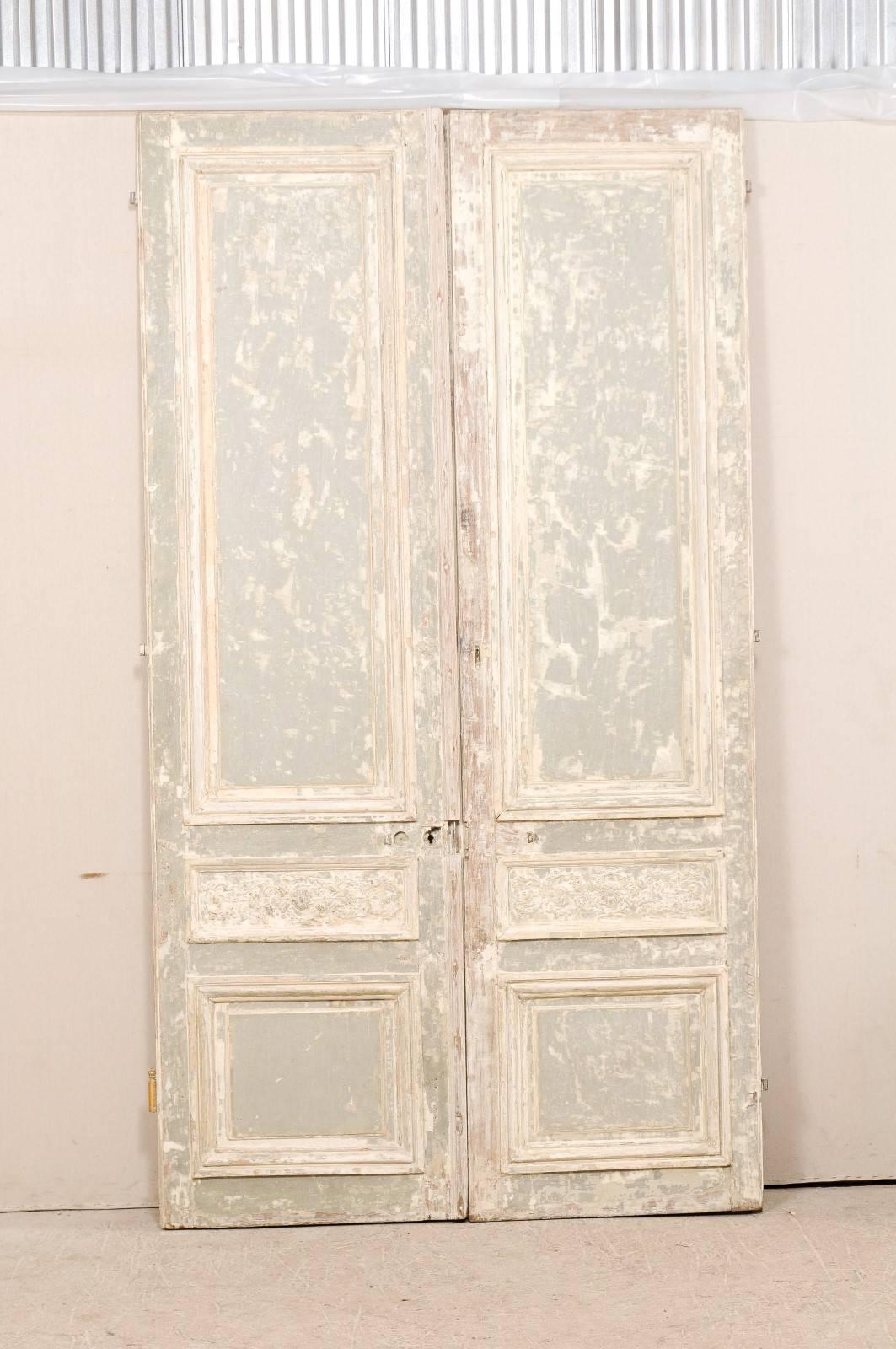 A tall pair of 19th century French doors. This exquisite pair of French doors each have three recessed panels on both sides, with the top panel being more elongated. The smaller middle panels of the front sides of these doors have an abundantly