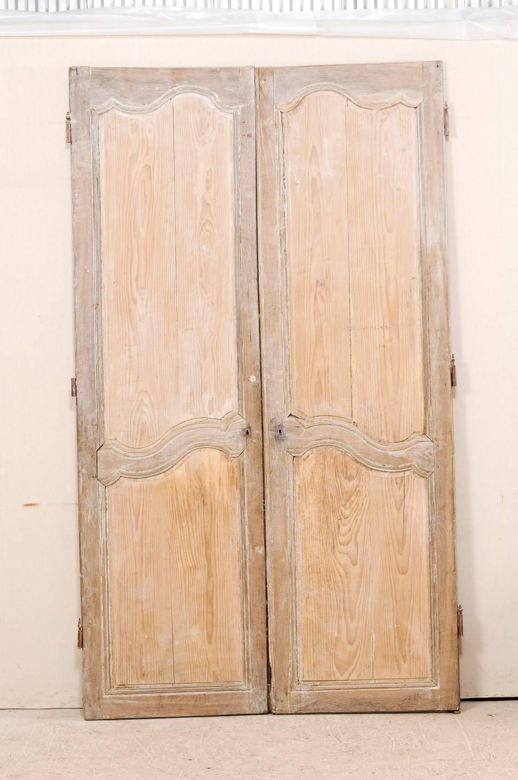 A pair of tall French wooden doors from the 19th century. This pair of French doors each feature two recessed panels, which have a sweetly carved curvy edging along the top and middle sections of the panel. The doors have a darker tone wood
