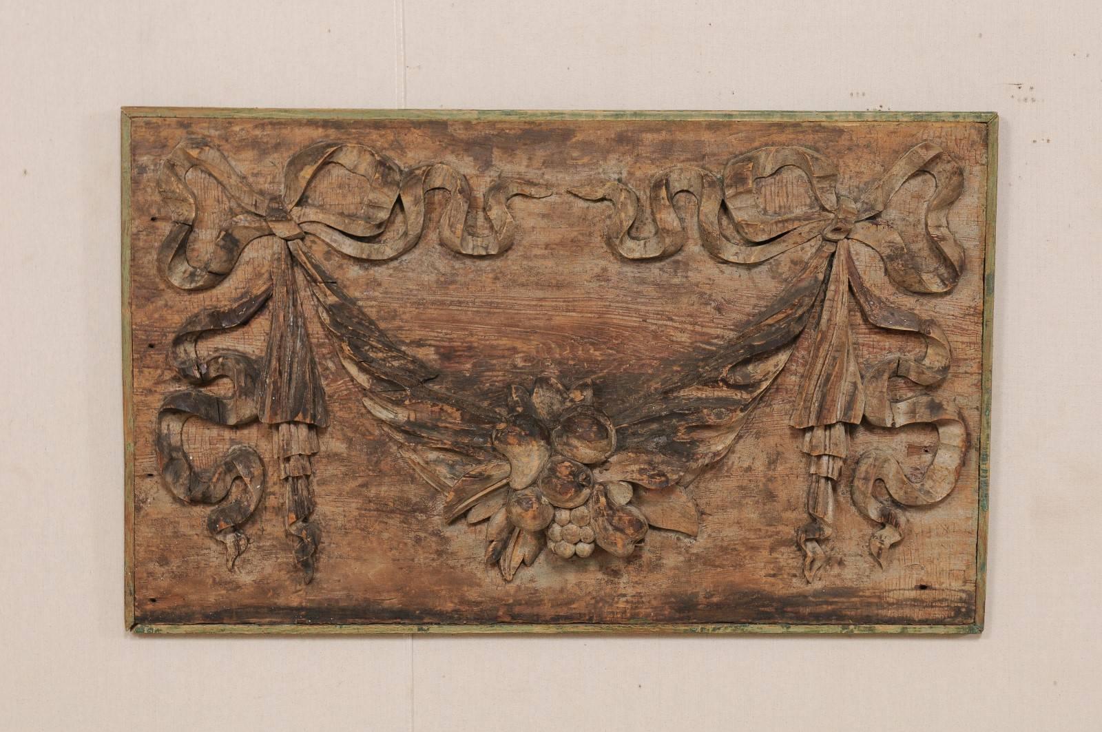 An Italian 19th century hand-carved wood plaque. This lovely Italian wall hanging plaque is oval shaped, made of wood, and features motifs of intricate bowed ribbons at each end with a swagged centrepiece filled with various fruits. This rich wood