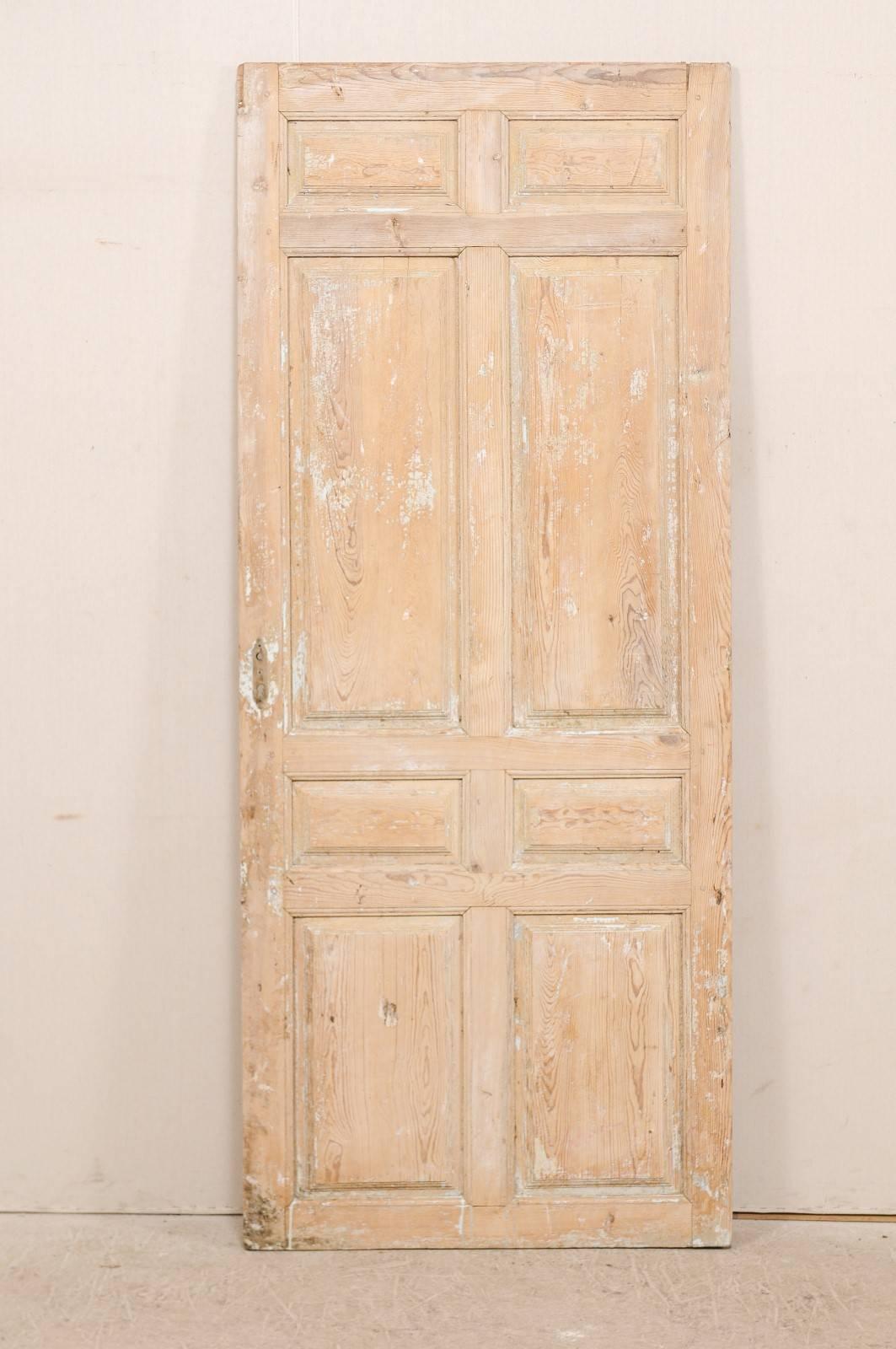 A single 19th century, French eight-panel wood door. This antique French door has eight recessed panels on both door sides, which alternate between smaller and longer rectangular shaped panels. The door has a natural wood finish with traces of old